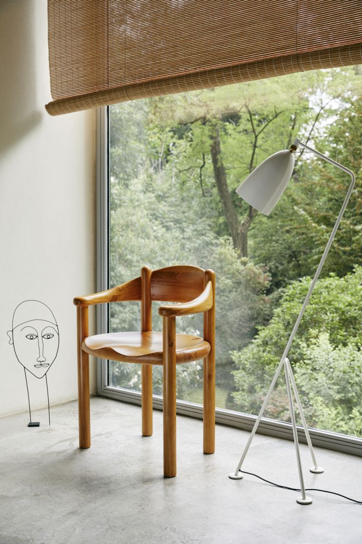 Daumiller Esszimmerstuhl von Gubi aus hellem Holz, minimalistisches Design mit Armlehnen vor Fenster und Stehlampe.