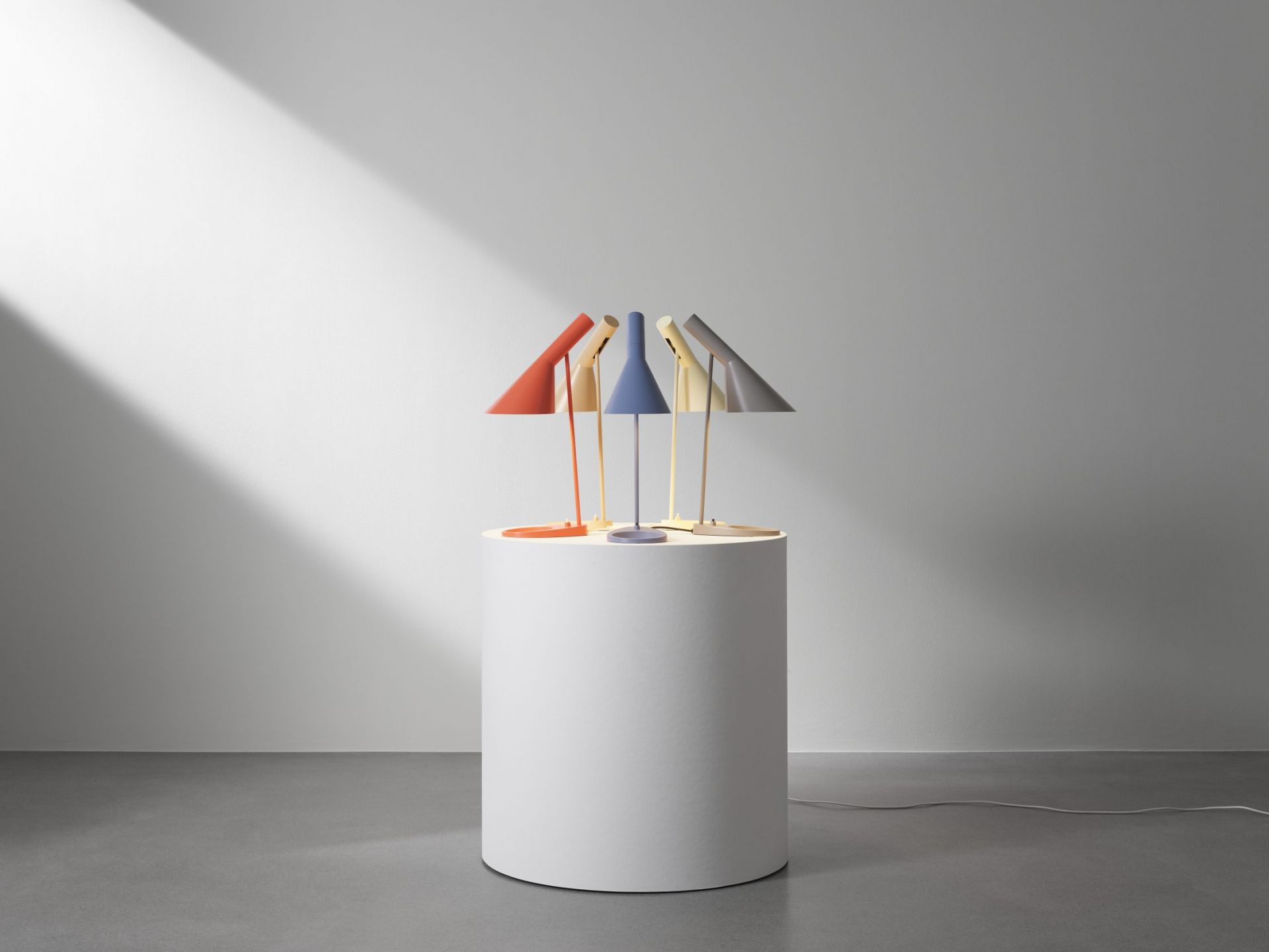 Mehrere Louis Poulsen AJ Tischleuchten in verschiedenen Farben auf einem Podest. Designklassiker.