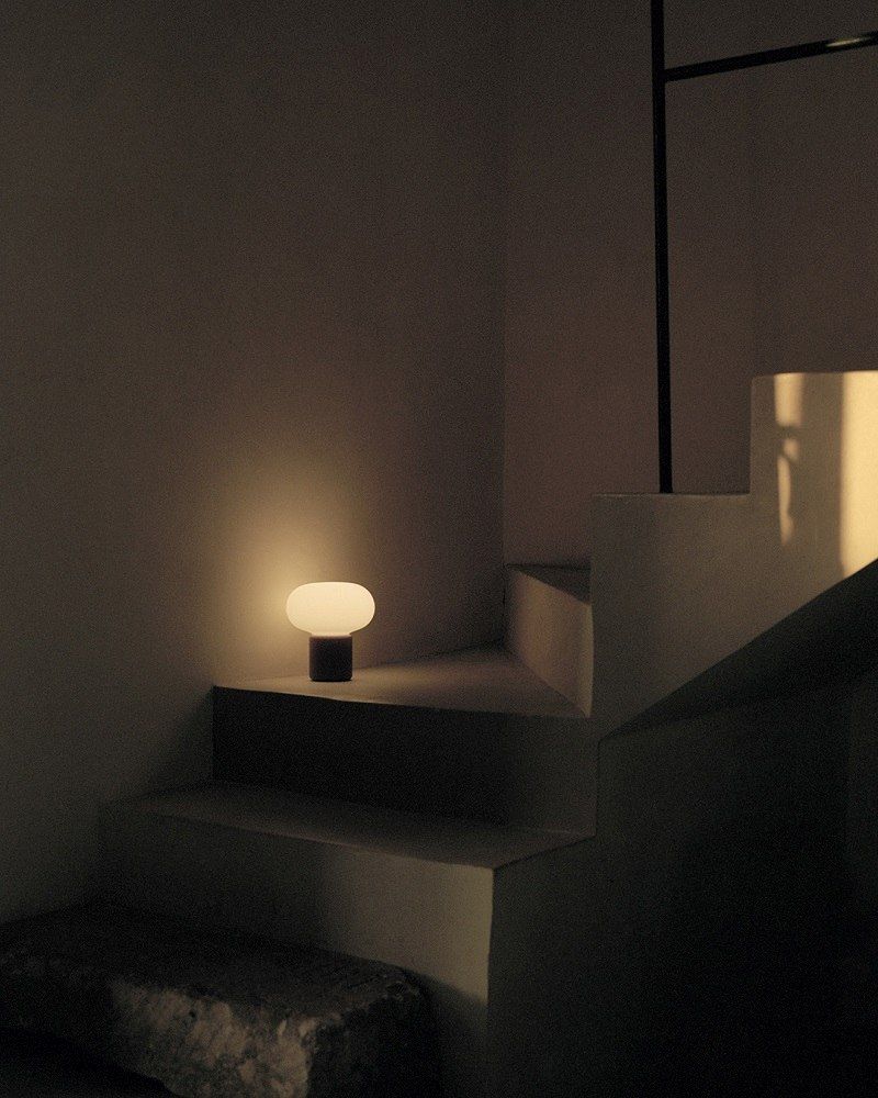 Ockergelbe Karl-Johan Tischleuchte von New Works auf einer Treppe, warmes, stimmungsvolles Licht.