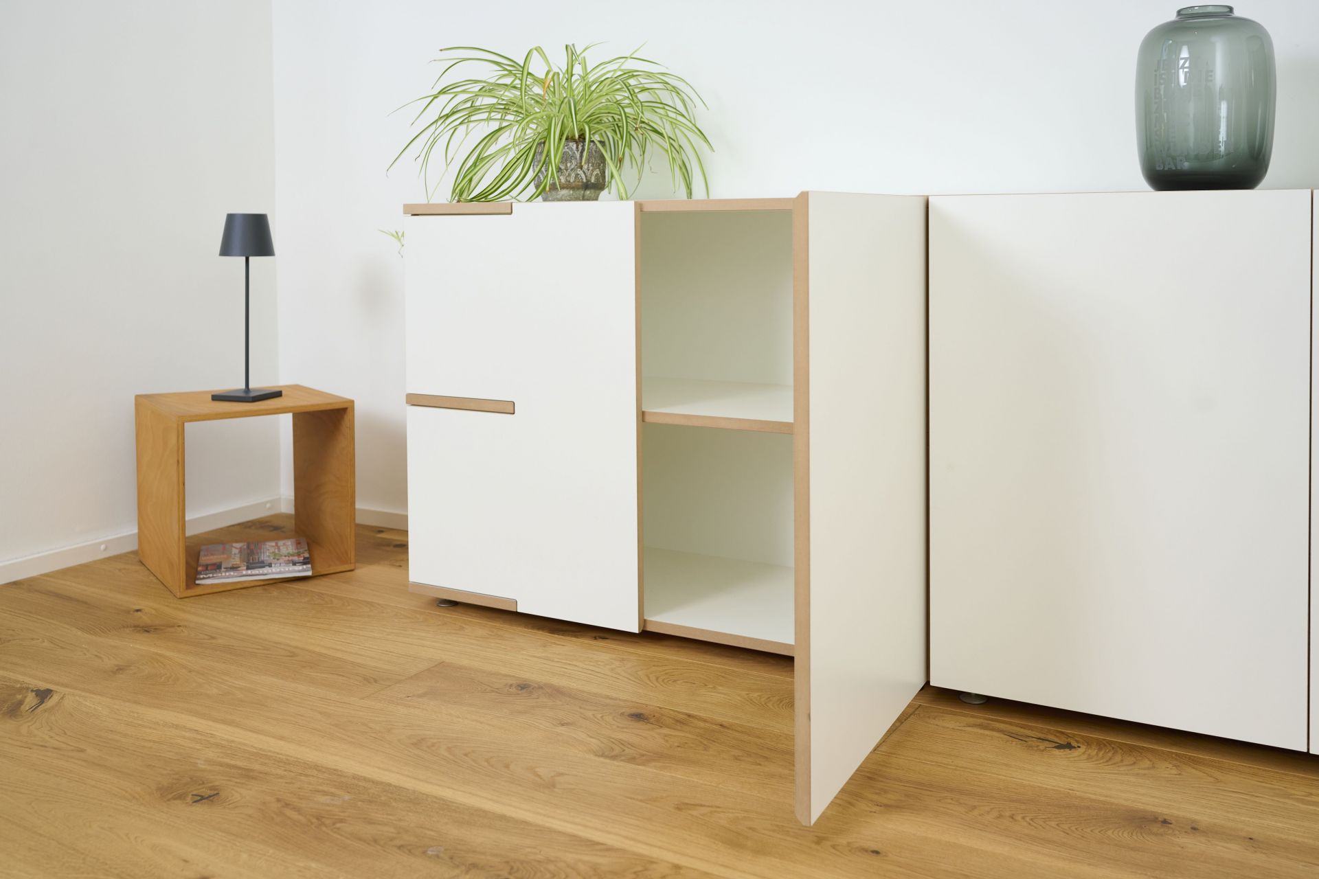 Tojo Stau Sideboard in Weiß mit offenen Regalen und Schranktüren auf Holzboden.