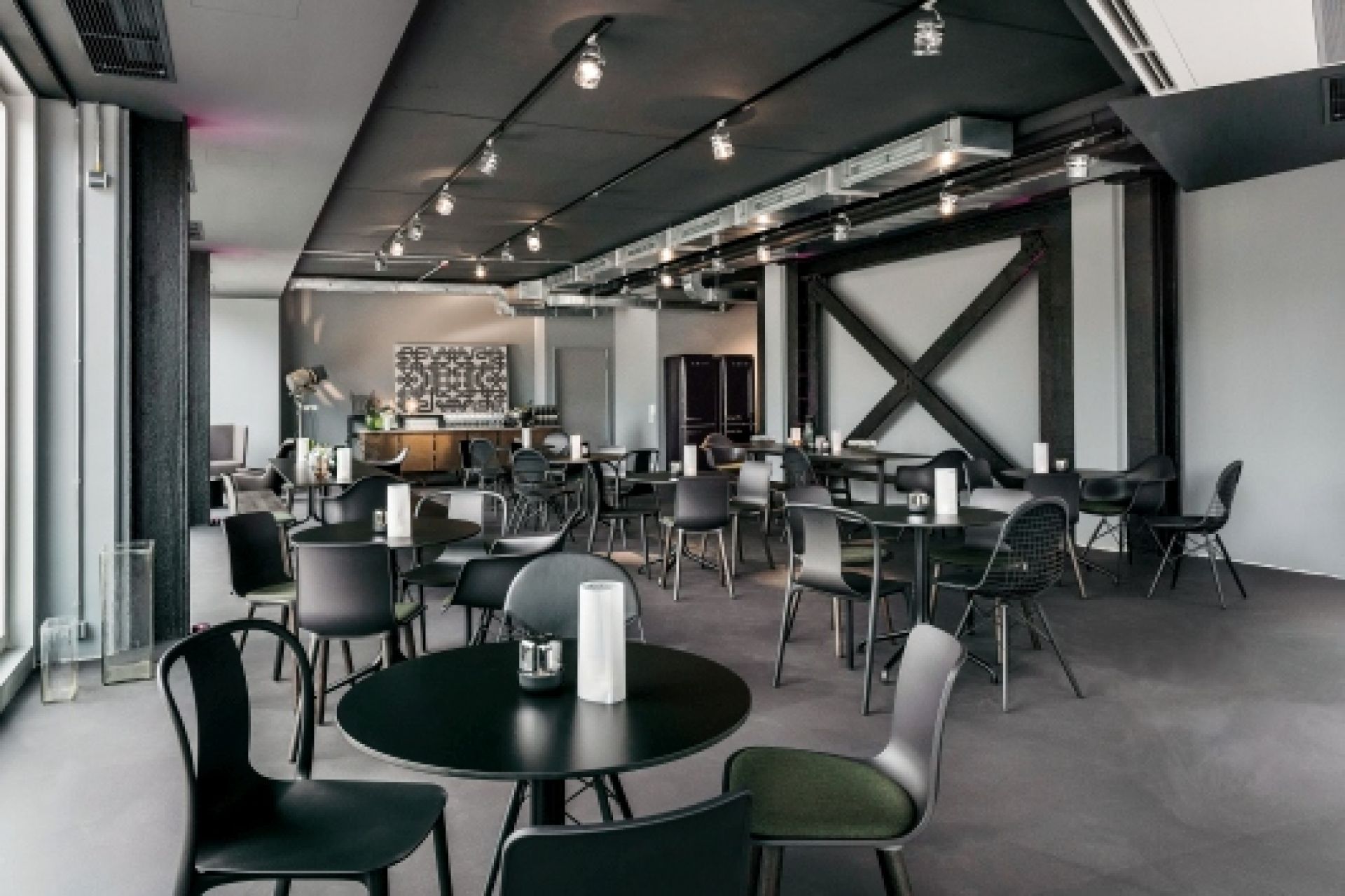Innenaufnahme eines Restaurants mit schwarzen Vitra Belleville Tischen und Stühlen auf dunklem Boden.