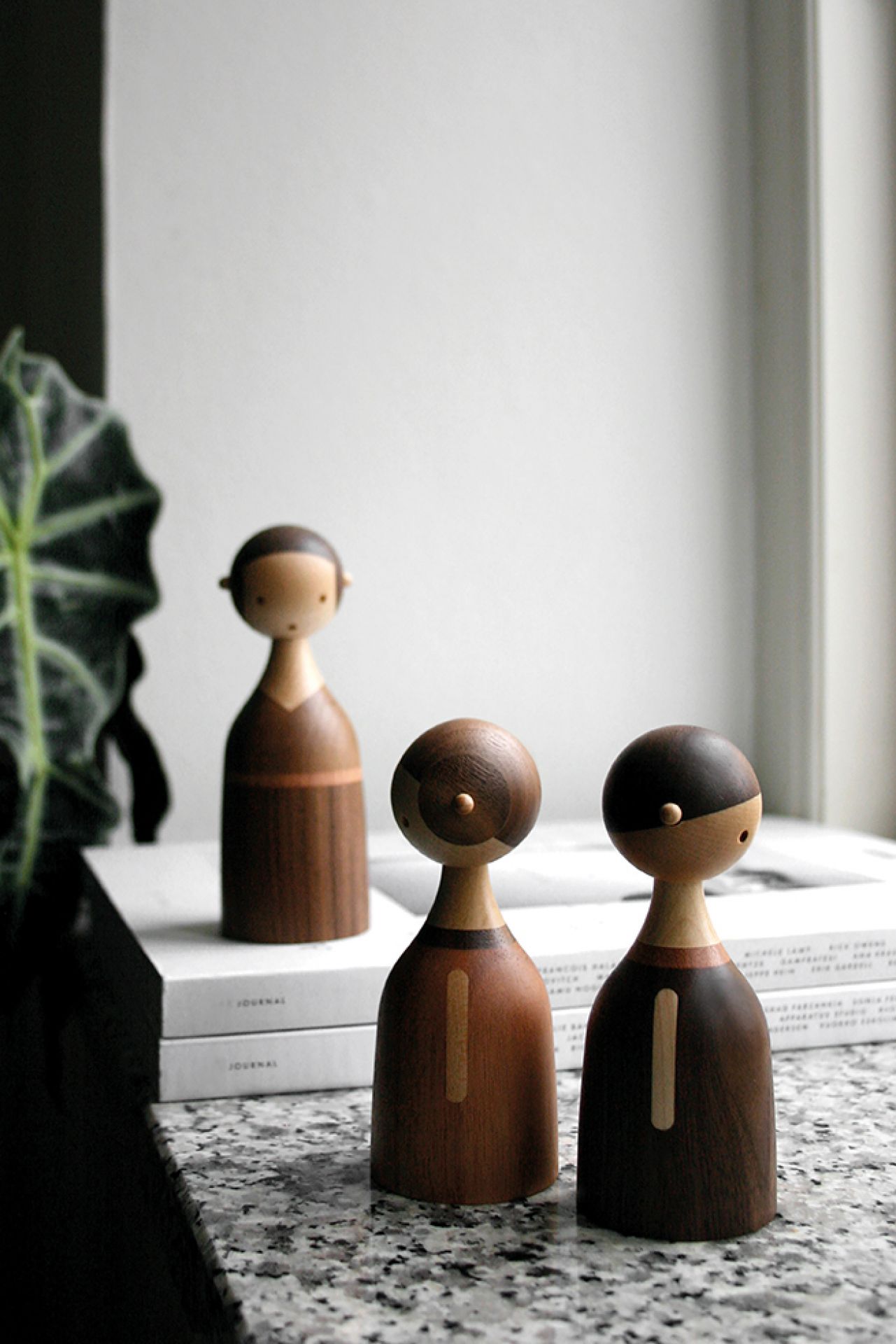 Drei Architectmade Holzfiguren, Kin Baby, auf einem Tisch vor einem Fenster. Dekorative Holzobjekte.