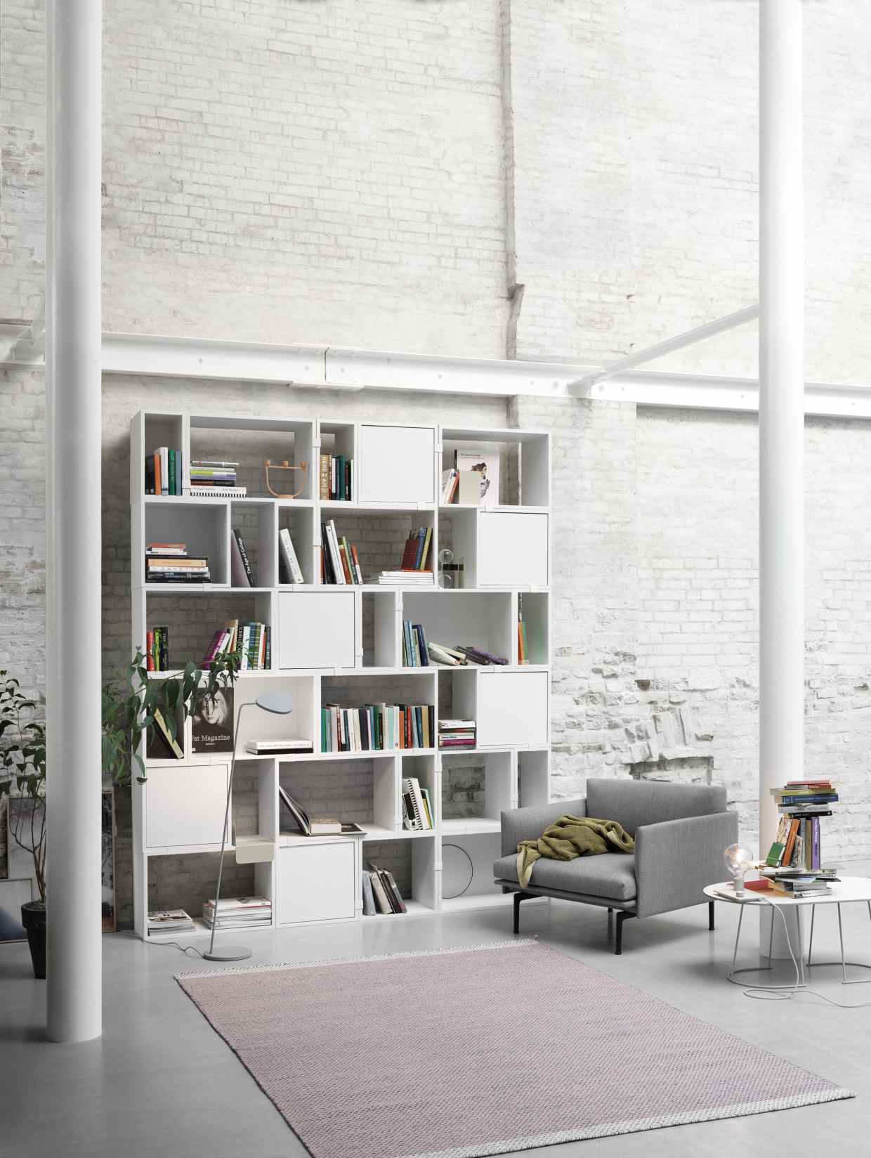 Muuto Stacked Storage System 2.0 Regalsystem in Weiß, kombiniert mit Bücher, Lampe, Sessel und Teppich.