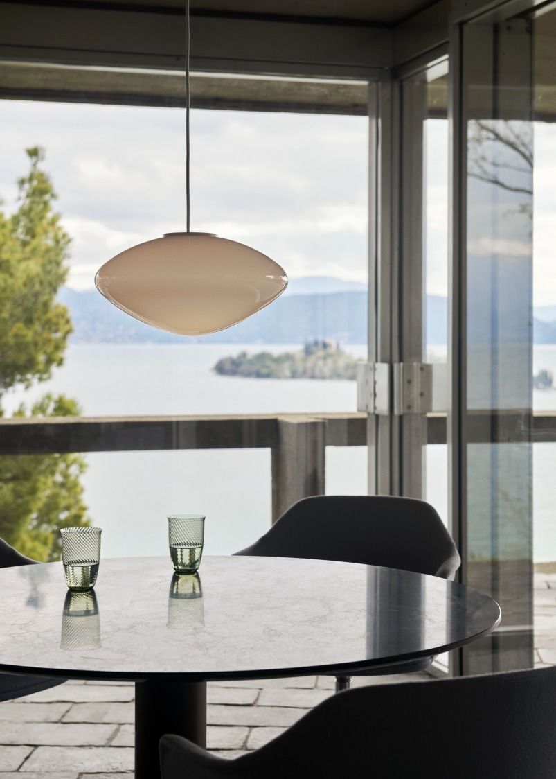 AndTradition Mist Pendelleuchte aus Opalglas über Esstisch mit Seeblick, modernes Design.