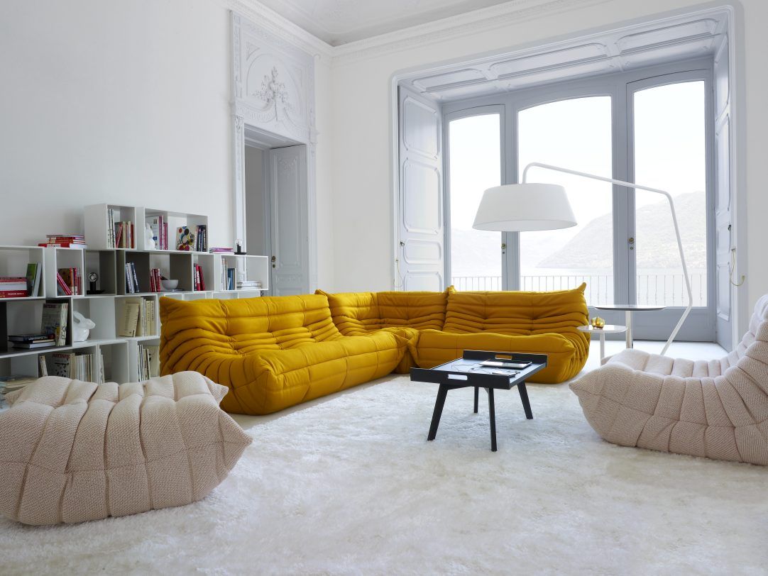 Gelber Togo Sofa-Klassiker von Ligne Roset mit passendem Hocker in modernem Wohnzimmer auf flauschigem Teppich.