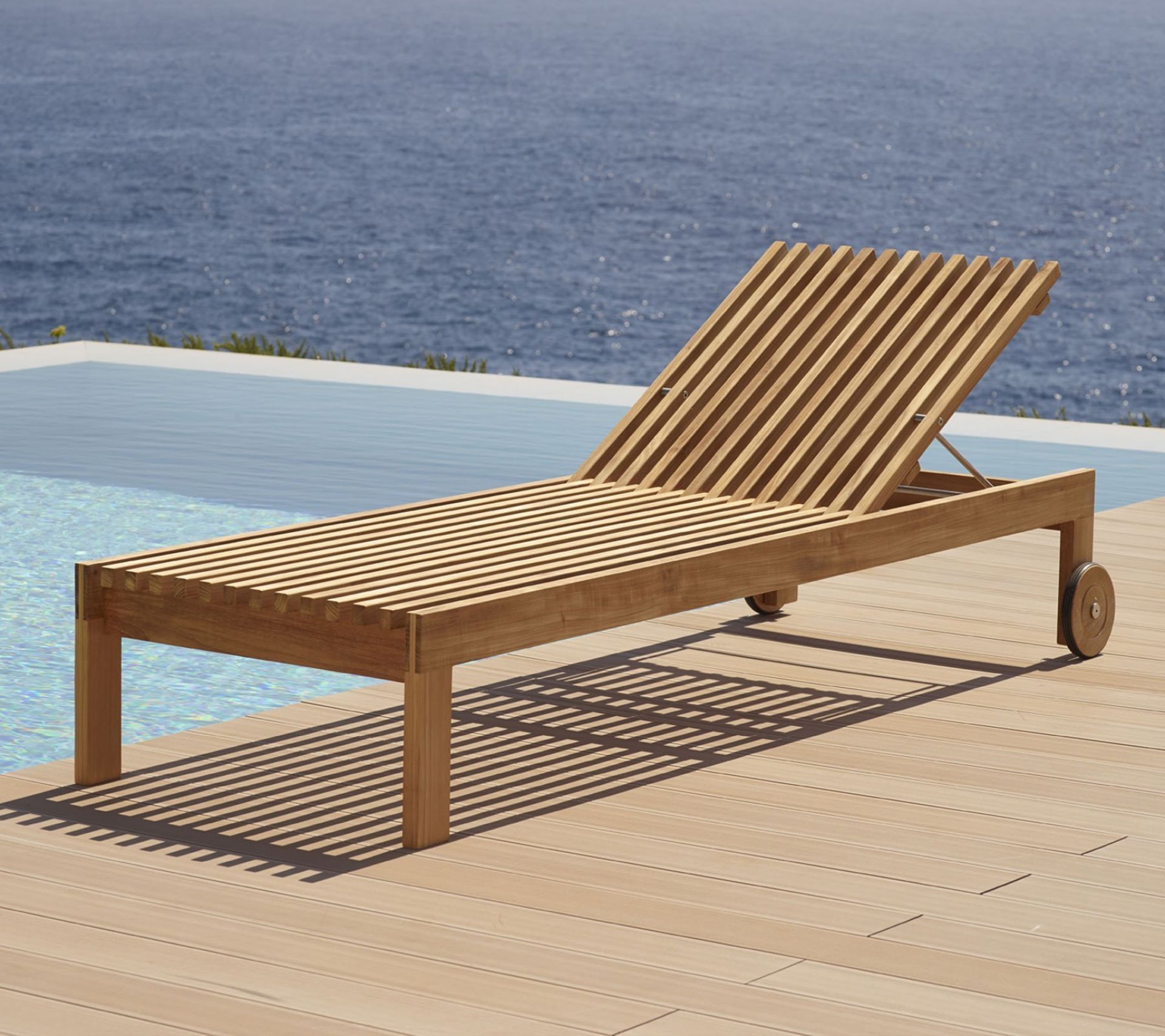 Amaze Sonnenliege von Cane-Line aus Teakholz am Pool mit Blick aufs Meer.