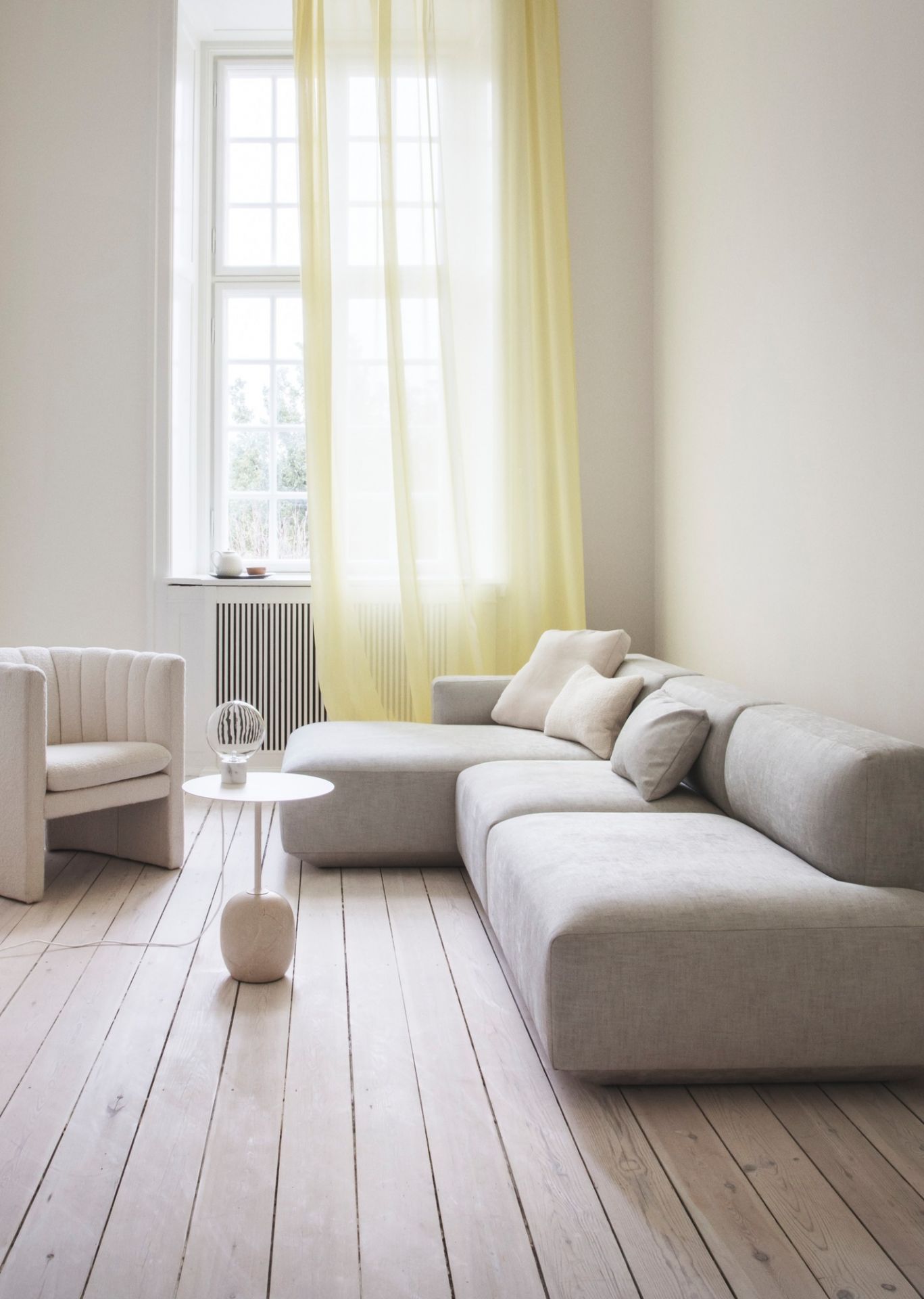 Moderner Wohnraum mit Lato Beistelltisch in Warm Schwarz neben Sessel und Sofa auf hellem Holzboden.