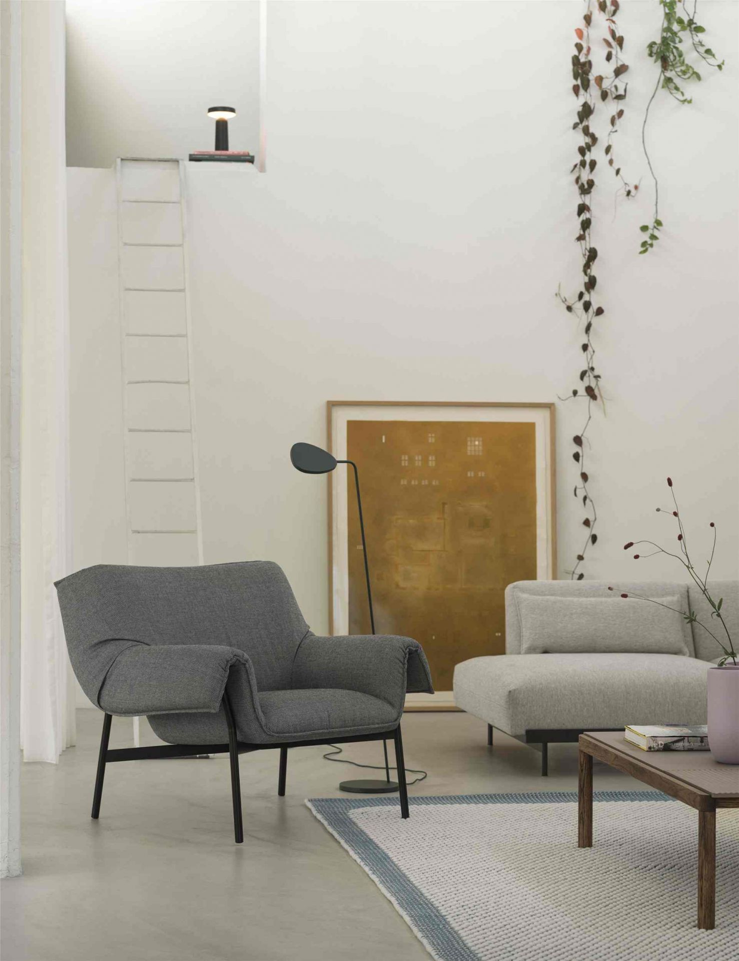 Wohnzimmer mit grauem Sessel, Sofa und Muuto Couchtisch aus Holz auf einem Teppich.