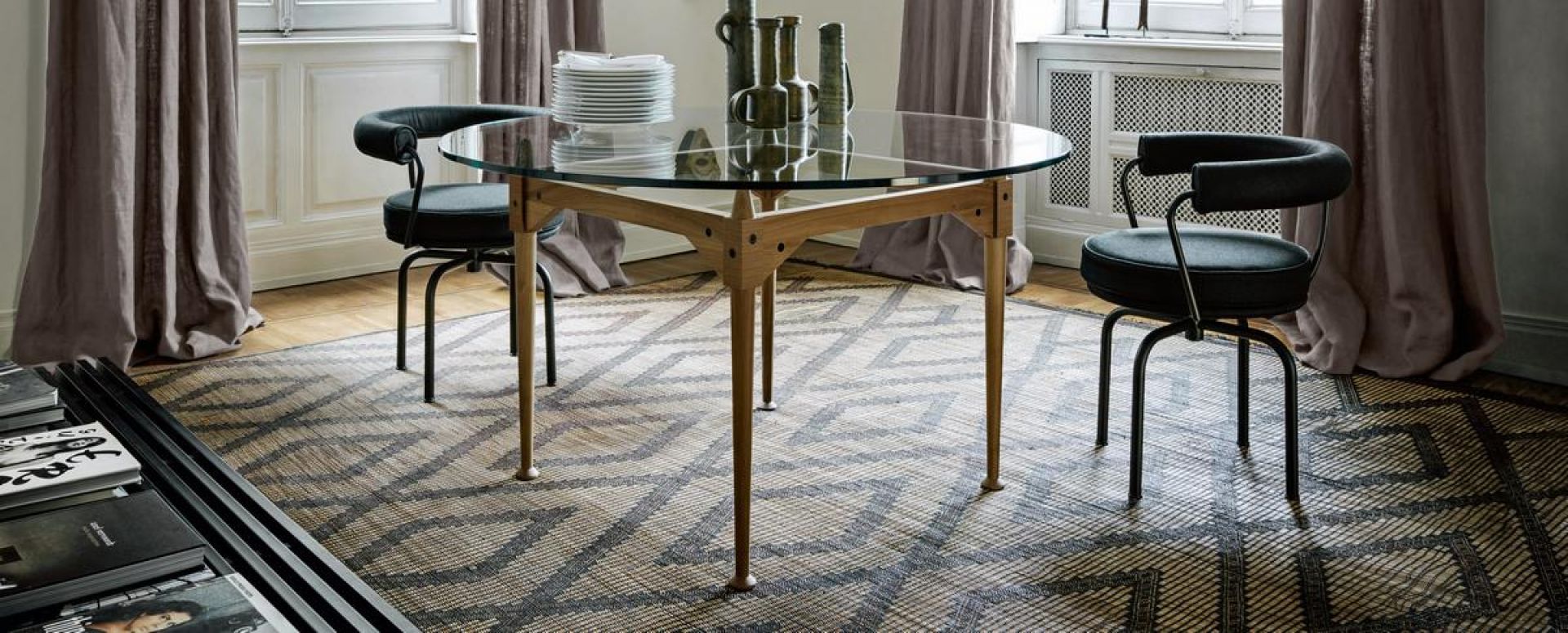 Esszimmer mit rundem Glastisch und zwei Cassina 7 Fauteuil Tournant Drehsesseln mit schwarzem Bezug.