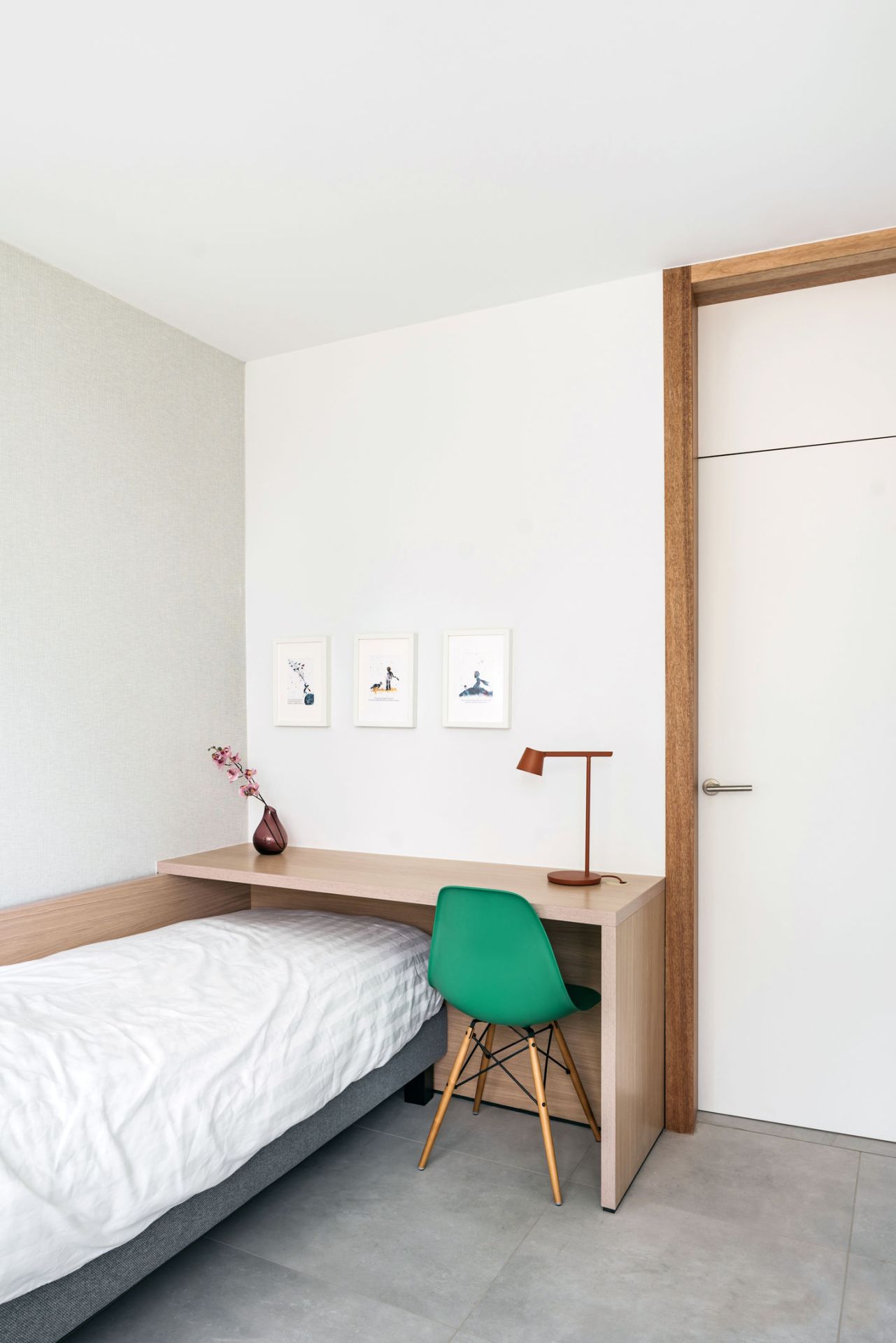 Heller Raum mit Bett, Schreibtisch und einem grünen Eames DSW Stuhl von Vitra.