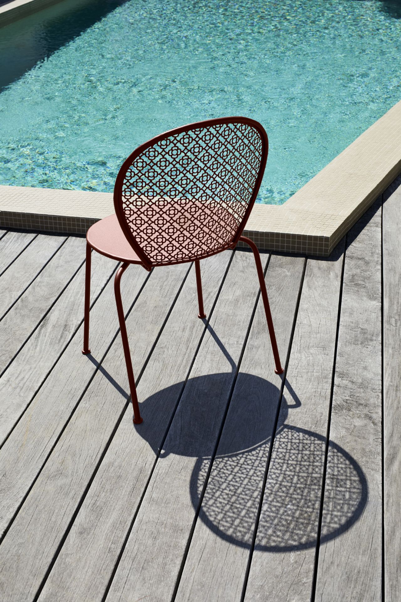 Lorette Stuhl von Fermob in Rotbraun auf Holzdeck neben Pool. Outdoor Möbel.