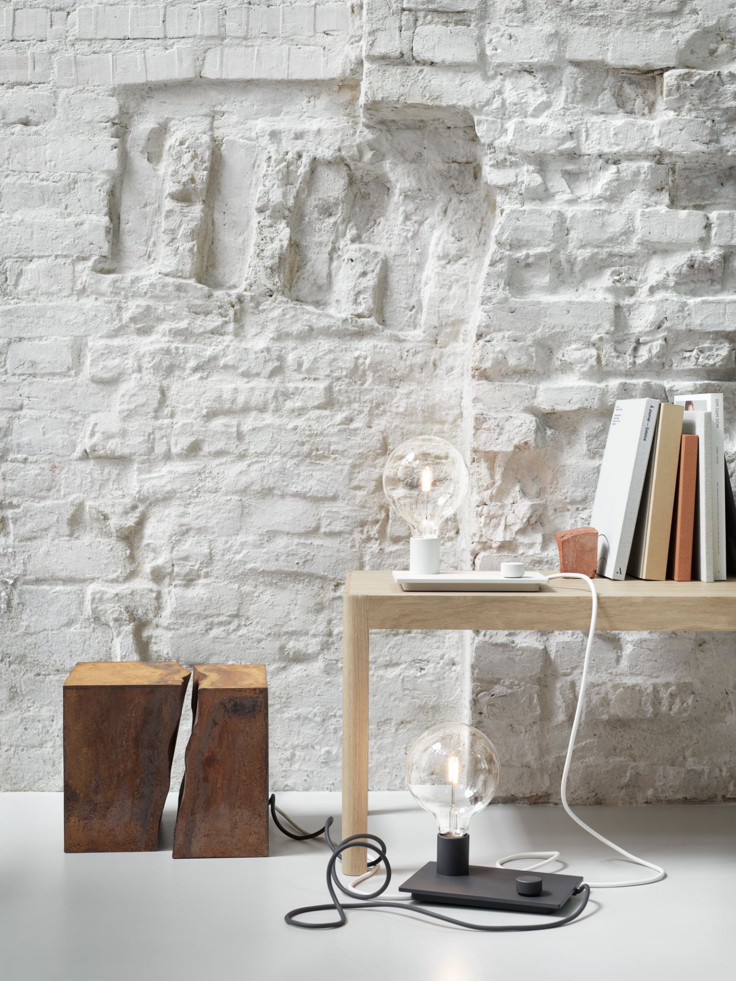 Muuto Workshop Table aus Eichenholz mit Lampe und Büchern vor einer weißen Backsteinwand.