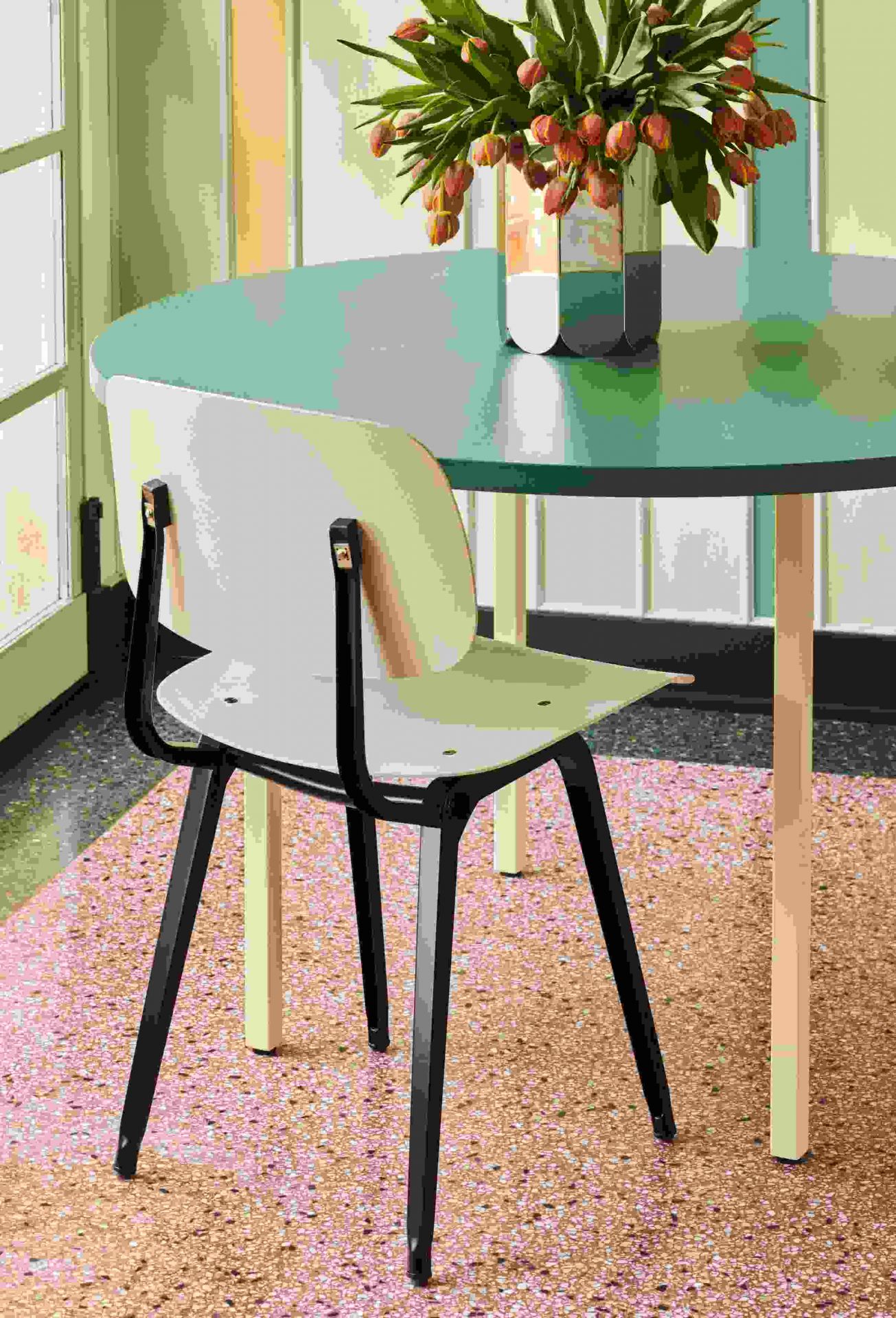 Arcs Vase L Mirror von Hay mit Tulpen auf einem runden Tisch neben einem Stuhl.