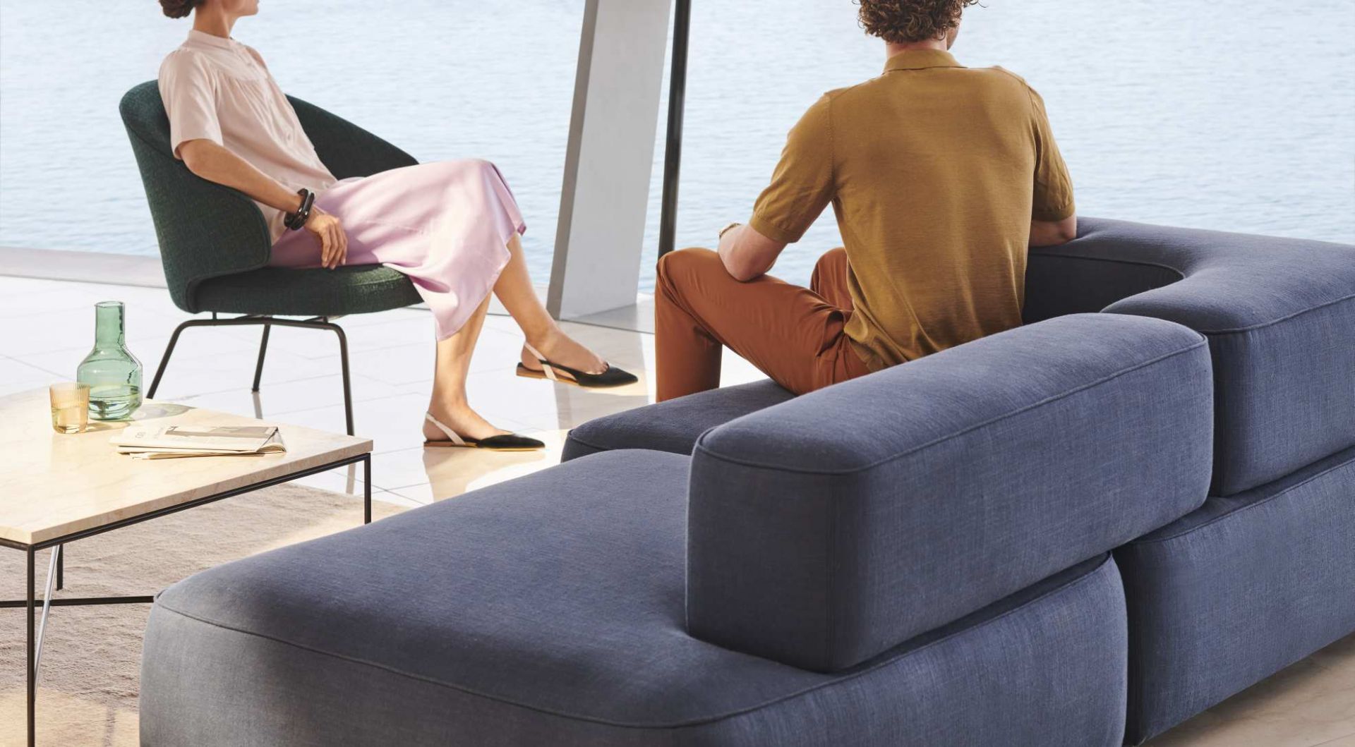 Person sitzt im Fritz Hansen Let Sessel und eine weitere Person auf einem modularen Sofa.