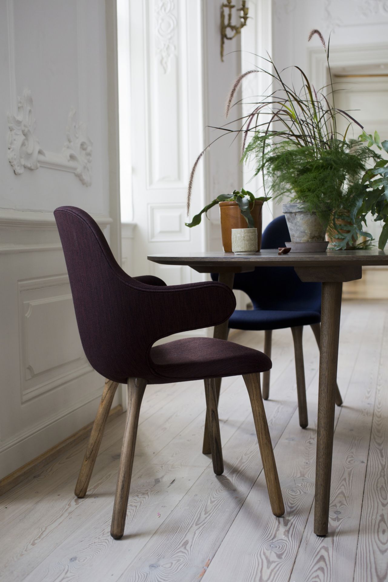 Nahaufnahme eines burgunderroten Catch Chair Stuhls von AndTradition mit Holzbeinen am Esstisch.