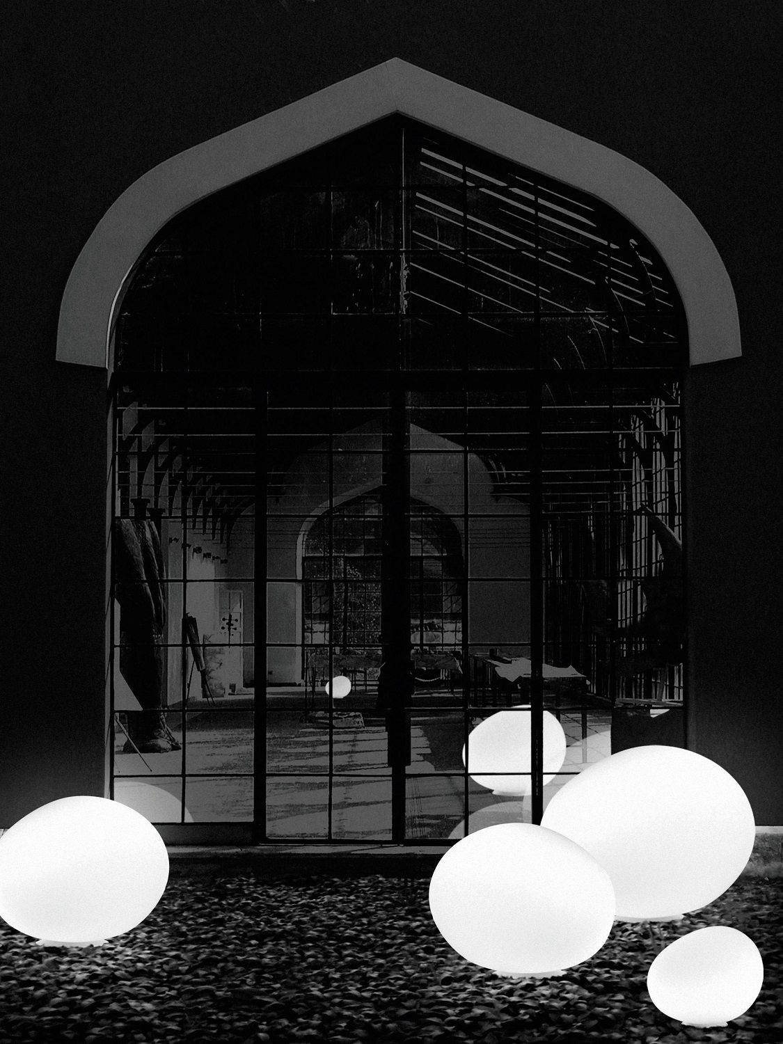 Gregg Outdoor Bodenleuchten von Foscarini, stilvolle Gartenbeleuchtung in Kieselform vor einem Fenster, Schwarz-Weiß.