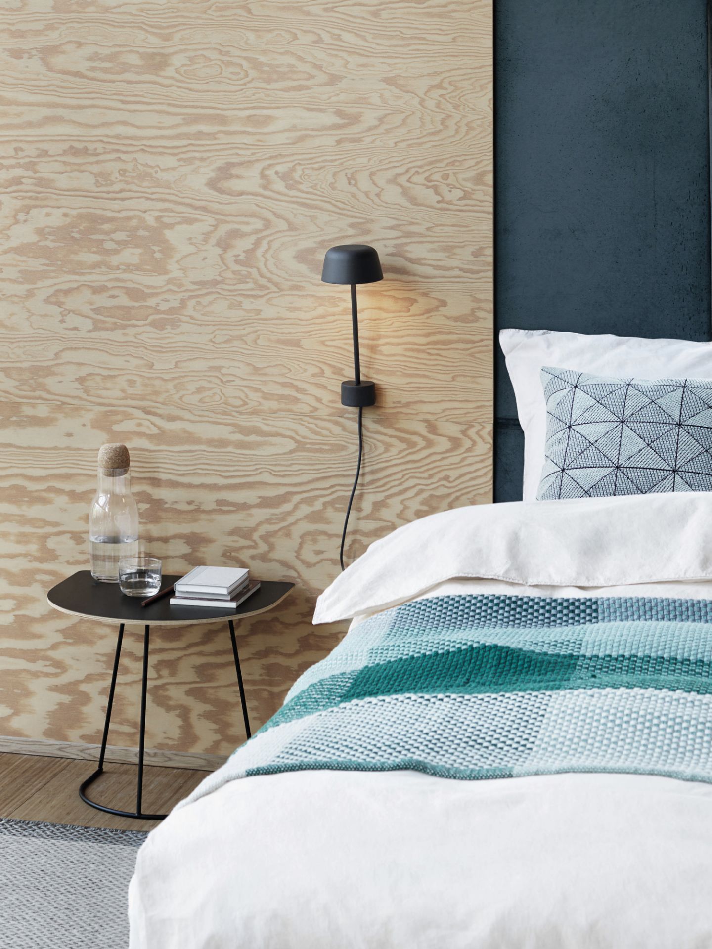 Schwarzer Airy Coffee Table Beistelltisch von Muuto neben einem Bett mit Wasserflasche und Büchern.