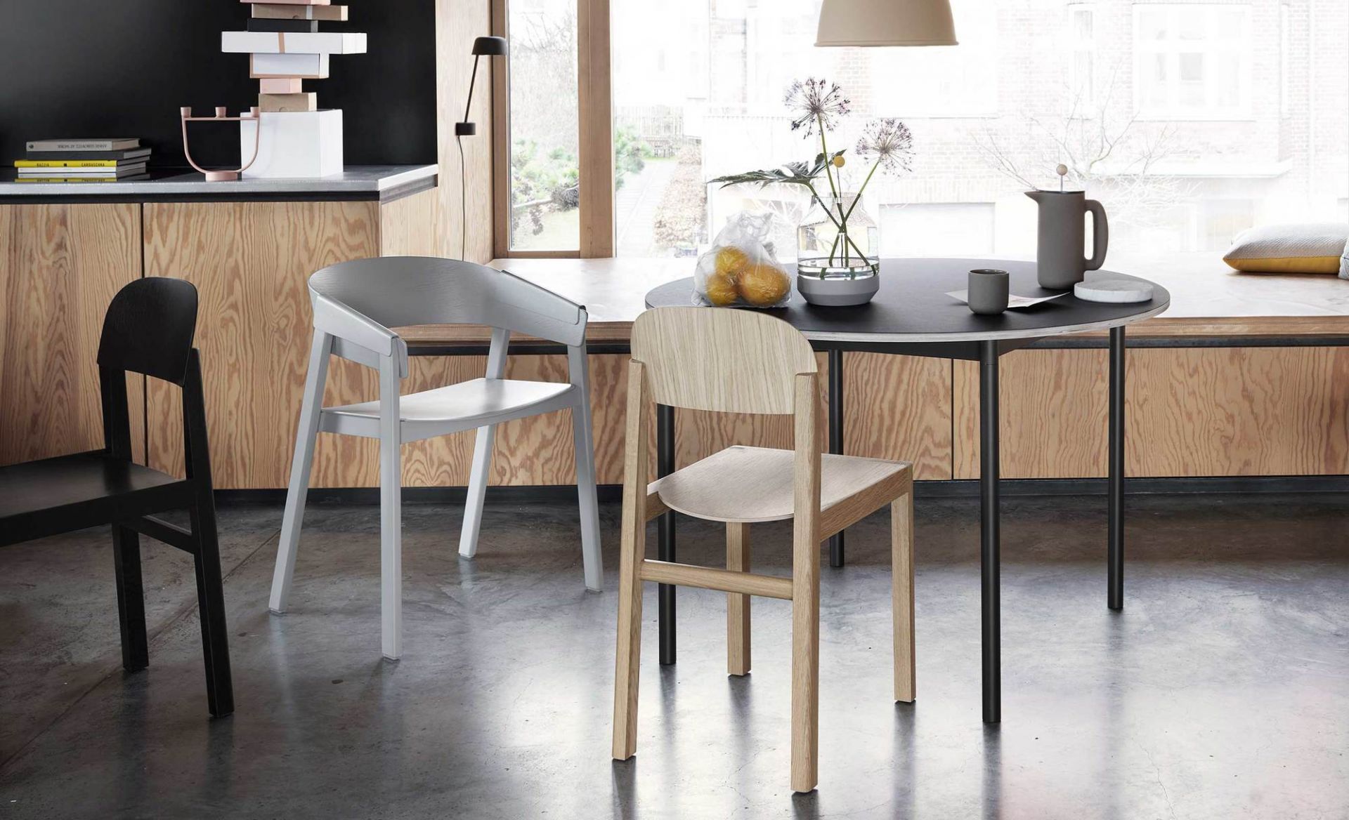 Muuto Base Table Round Tisch mit Stühlen in modernem Esszimmer, schwarze Tischplatte, Holzstühle.