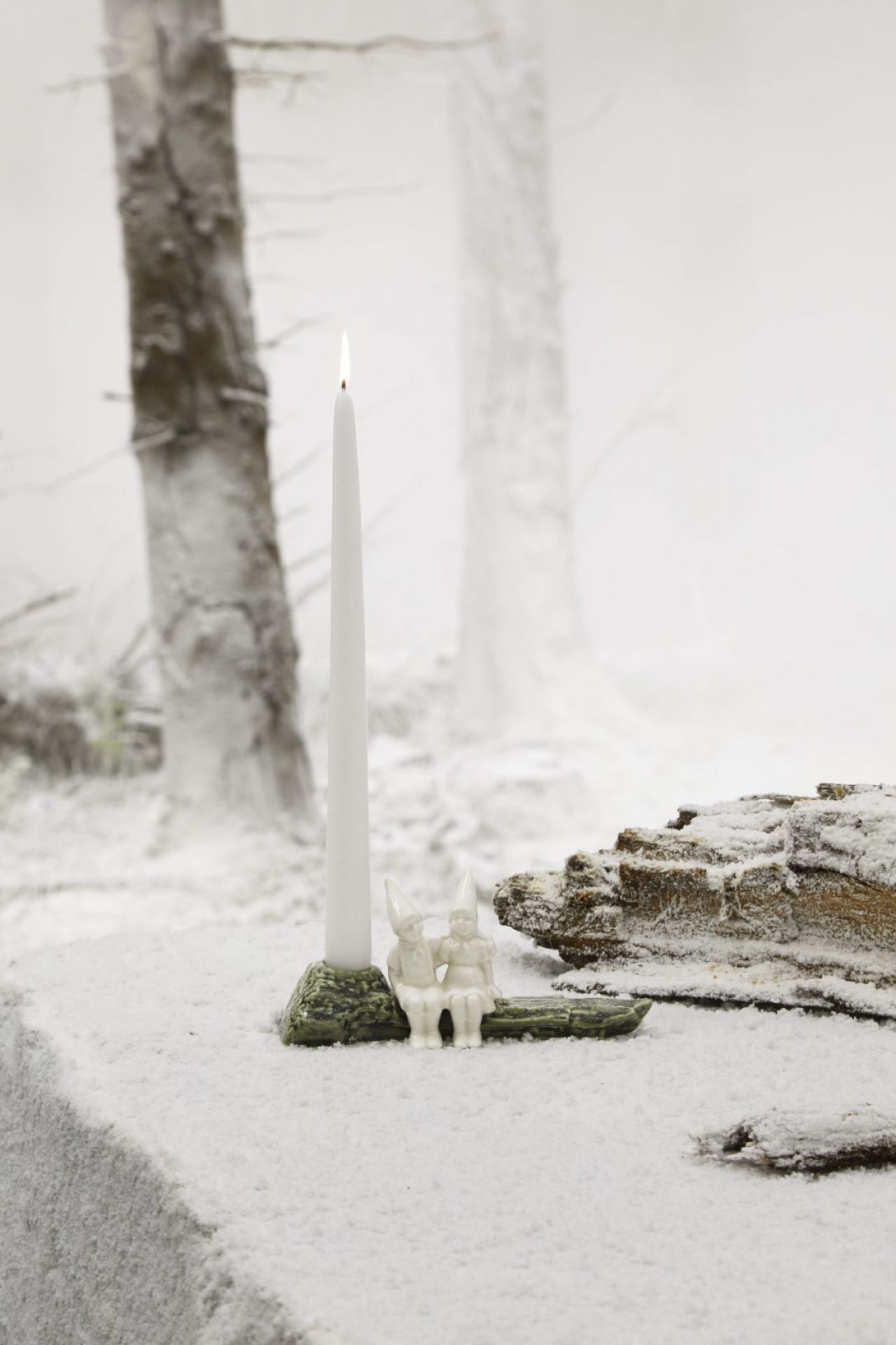Christmas Tales Julekram Kerzenständer mit brennender, weißer Kerze und zwei kleinen Figuren im winterlichen Schnee.