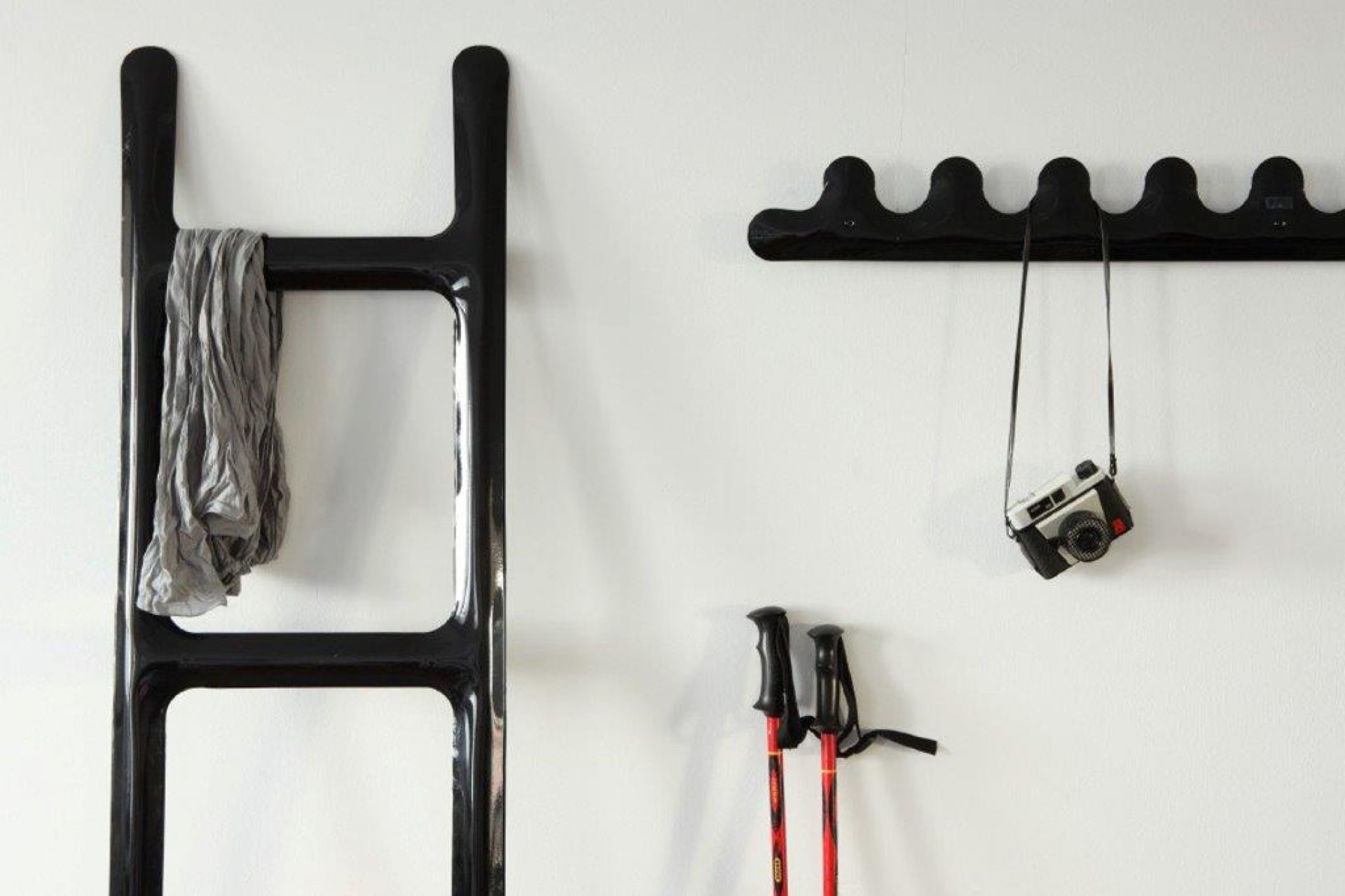 Schwarzer Zieta Herrendiener mit Schal, Hakenleiste mit Kamera und Skistöcke an weißer Wand.