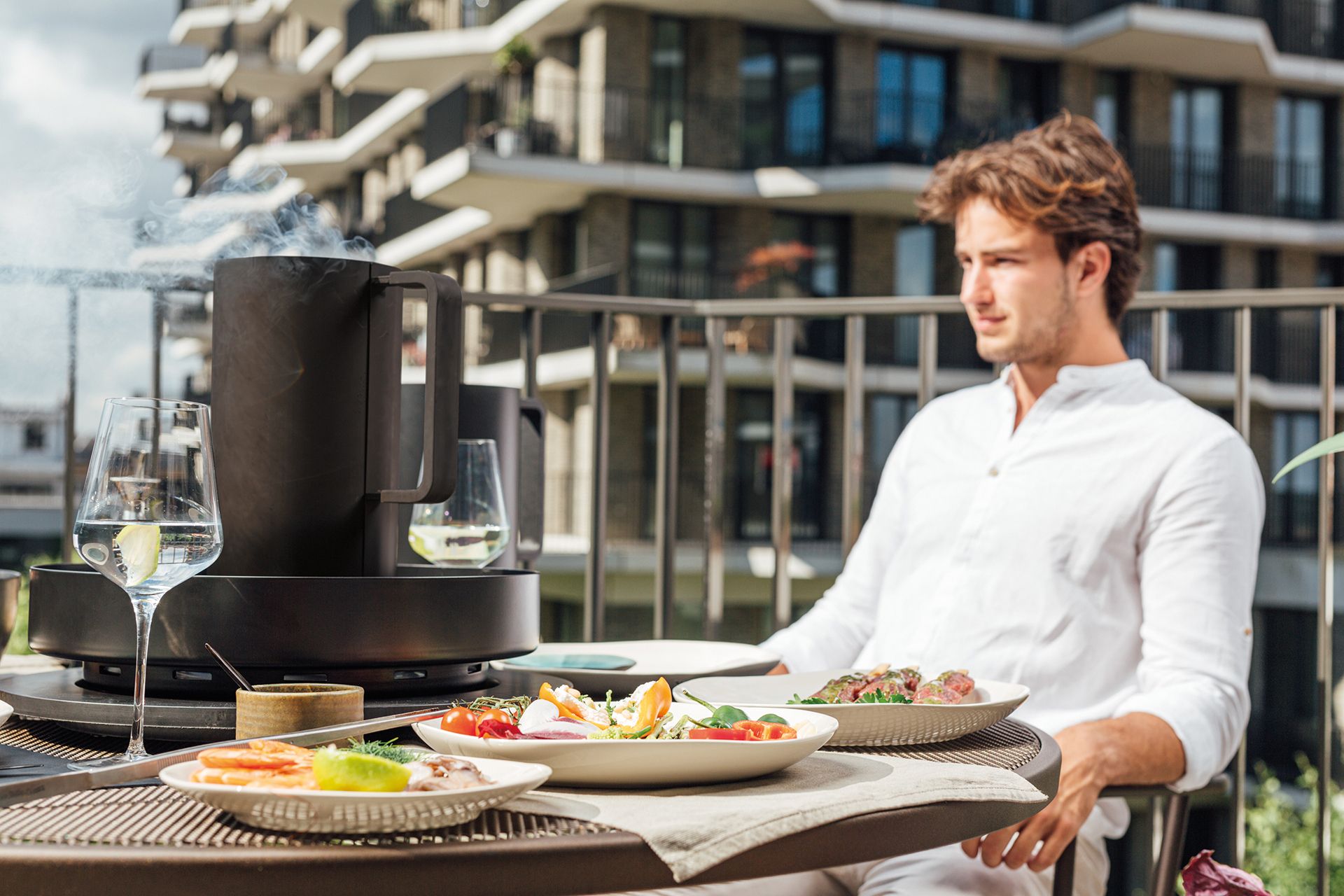 Tabl'O Tischgrill von Ofyr auf einem Balkon mit Speisen und Getränken, Mann im Hintergrund.