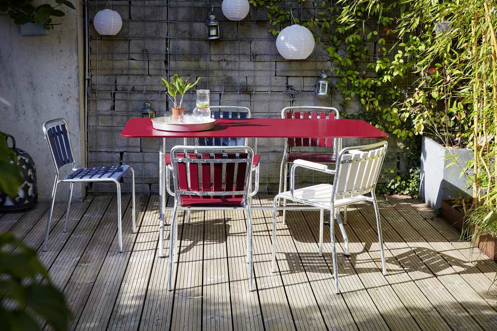 Roter Gartentisch mit vier Haefeli Stühlen von Embru auf einer Holzterrasse im Außenbereich.