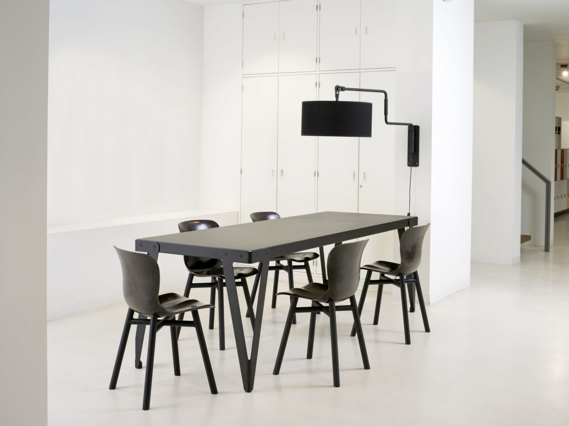 Schwarzer Lloyd Indoor Table Tisch Functionals mit passenden Stühlen und Lampe in minimalistischem, weißem Raum.