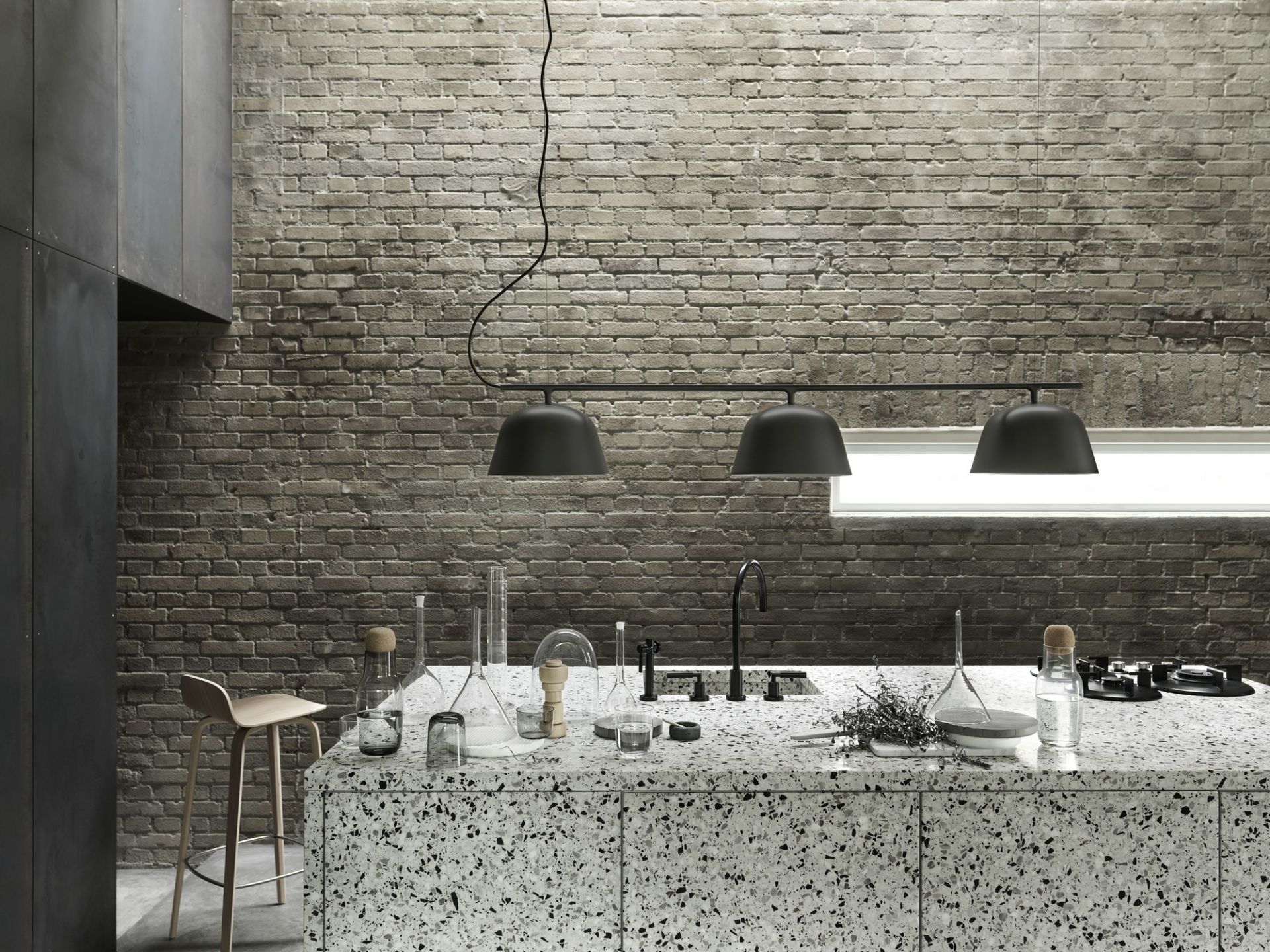Moderne Küche mit Ambit Rail Pendelleuchte von Muuto, drei mattschwarze Lampenschirme über einer Kücheninsel.