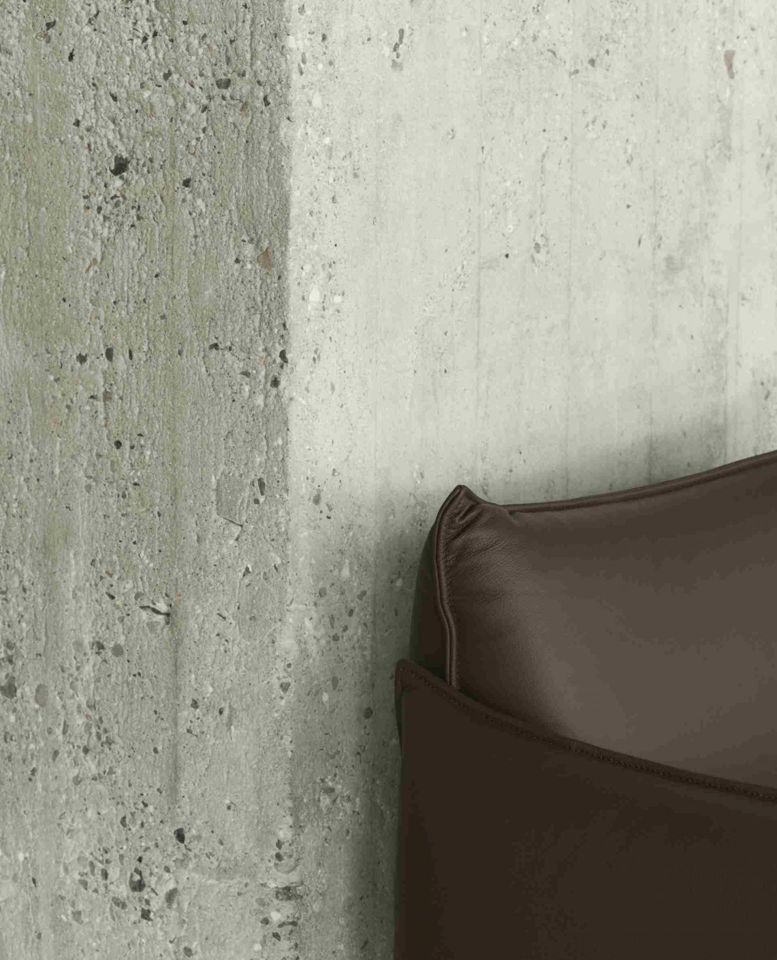 Detailaufnahme des braunen Ark Lounge Sessels von Normann Copenhagen vor einer grauen Betonwand.