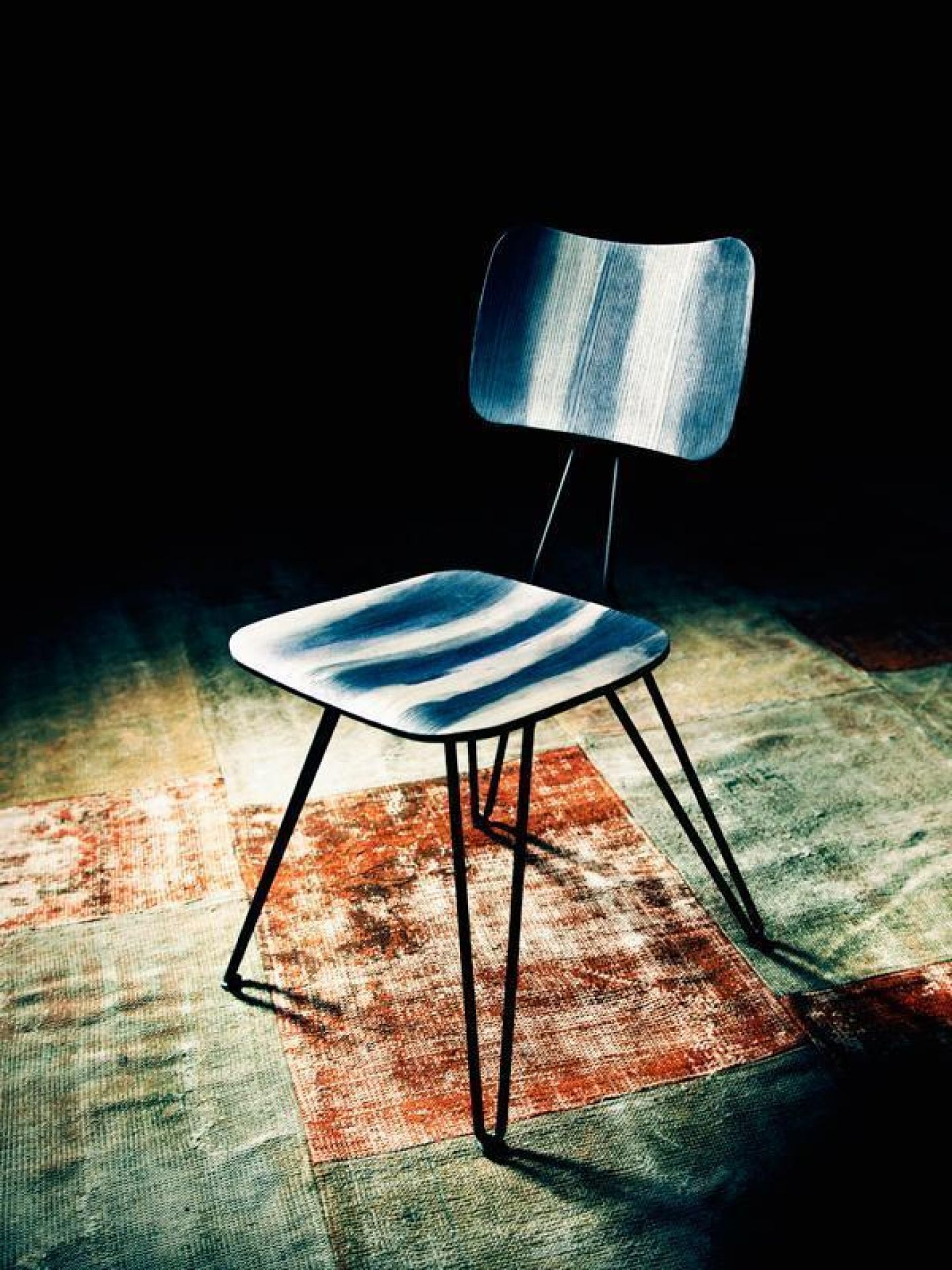Moderner Esszimmerstuhl mit blau-weiß gestreiftem Bezug und schwarzen Metallbeinen auf einem Patchwork-Teppich.