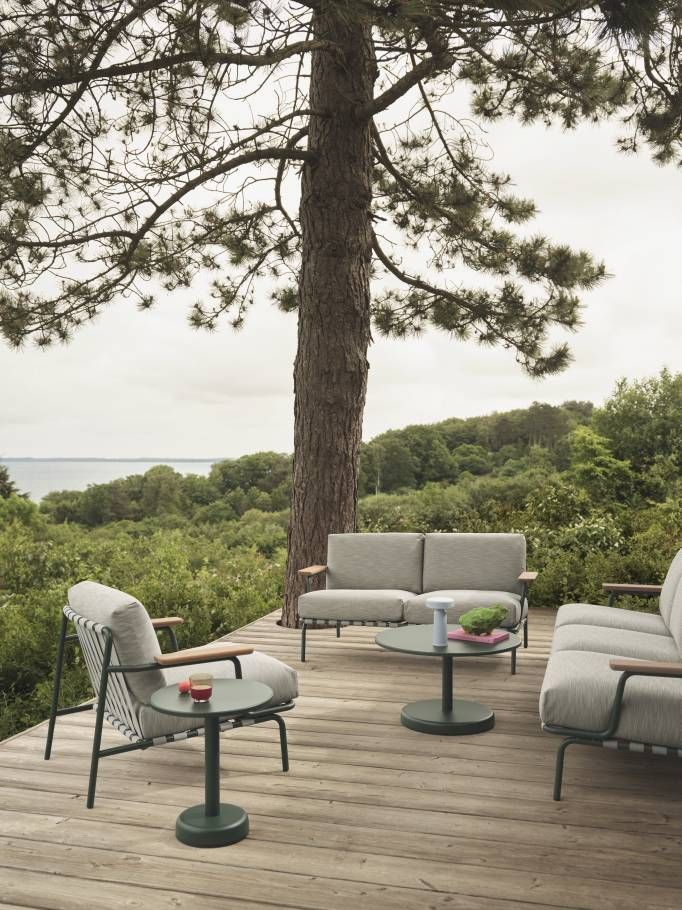 Muuto Settle Outdoor Sofa 2-Sitzer auf Holzterrasse mit Meerblick, umgeben von grüner Natur.