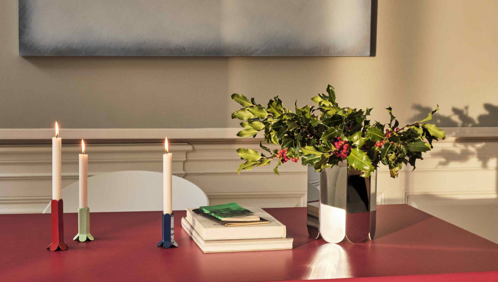 Nahaufnahme der Hay Arcs Vase L Mirror, gefüllt mit Stechpalmenzweigen, auf einem roten Tisch mit Kerzenständern.