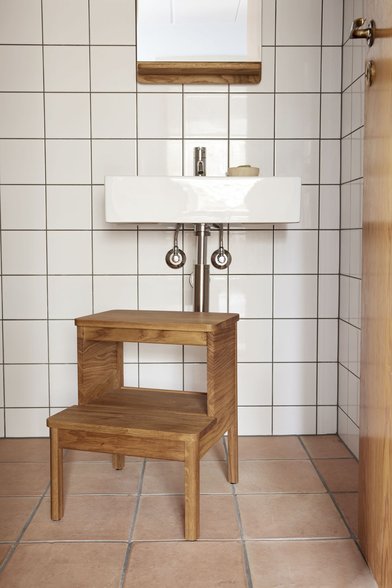 A Line Steighocker von Form & Refine aus Eichenholz im Badezimmer vor einem Waschbecken.