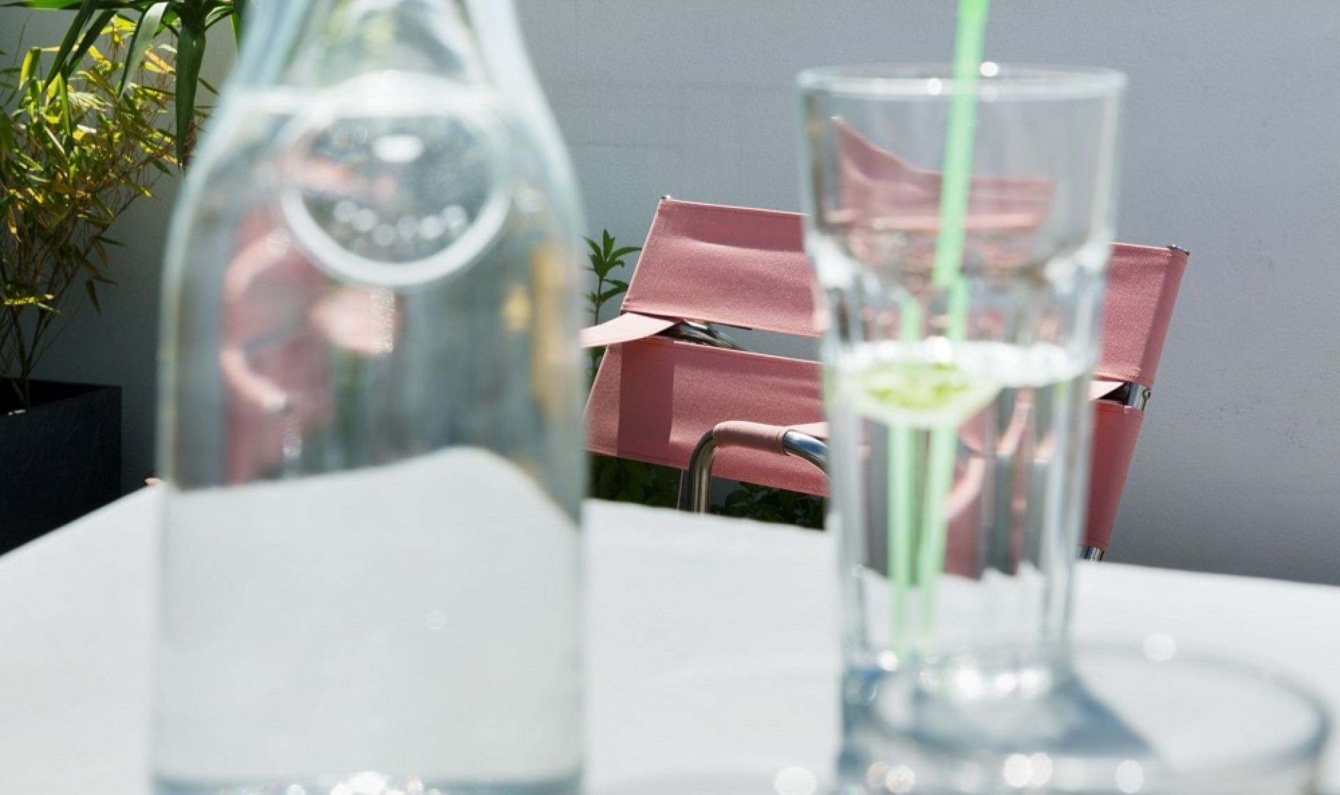 Nahaufnahme: Tecta D4 Bauhaus Faltsessel in Rosa, gesehen durch Wasserflasche und Glas mit Strohhalm.