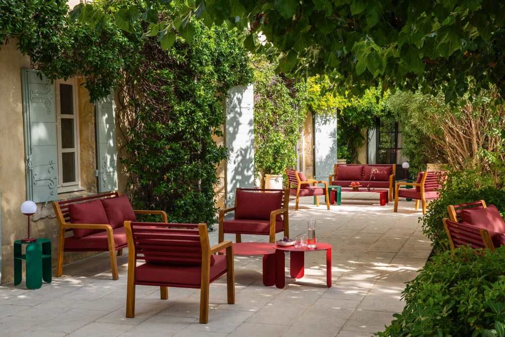 Fermob Somerset Sessel und Outdoor-Möbel-Set in Rot und Holz auf einer Terrasse im Garten.