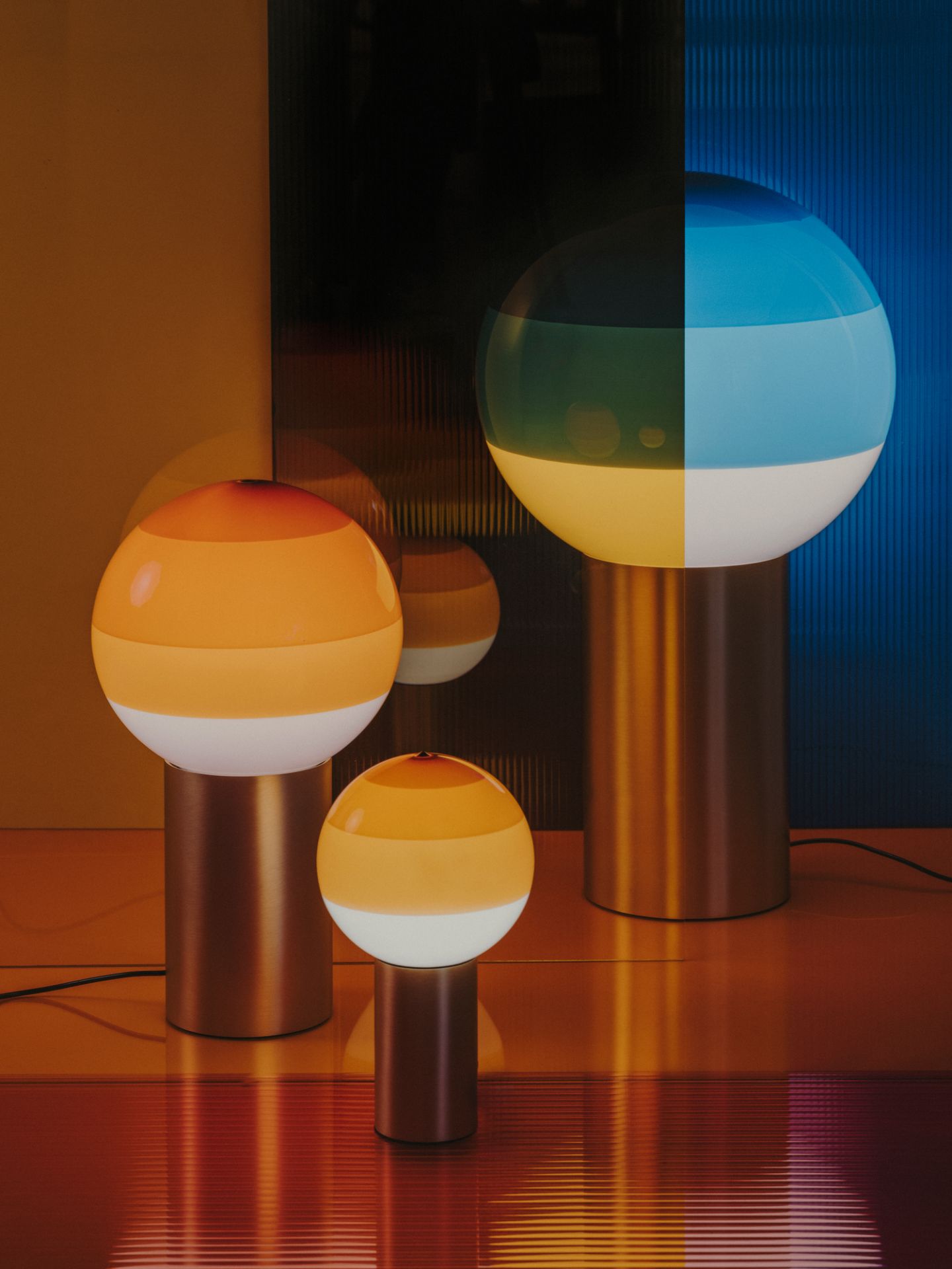 Drei Marset Dipping Light Tischleuchten in verschiedenen Größen und Farben auf glänzender Oberfläche.