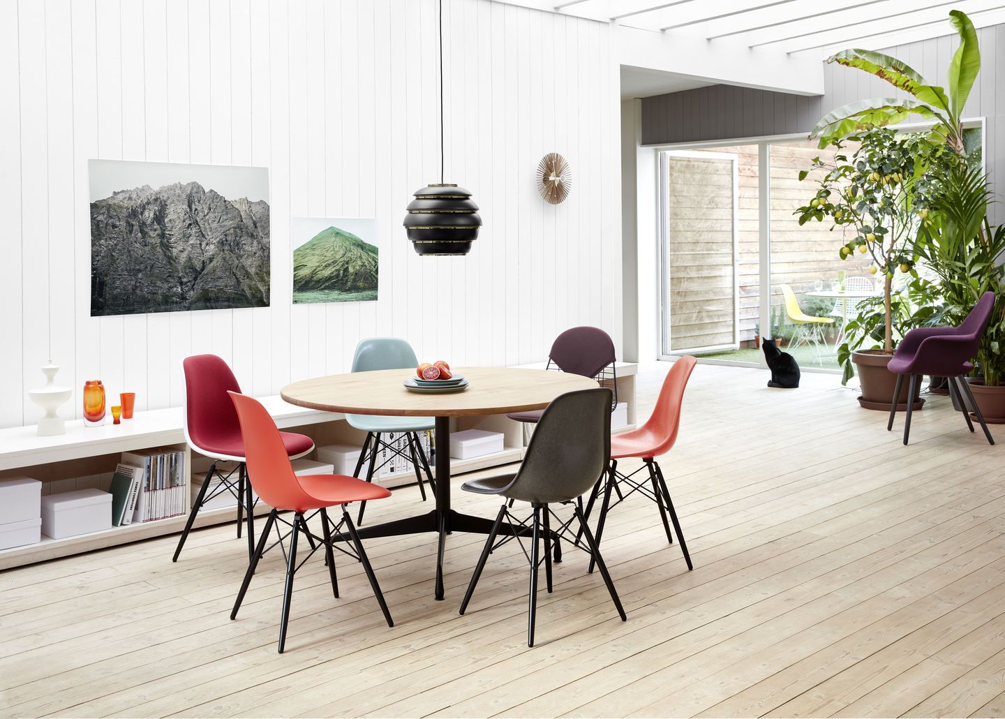 Esszimmer mit rundem Holztisch und farbenfrohen DKW Wire Chairs von Vitra mit Sitzkissen.