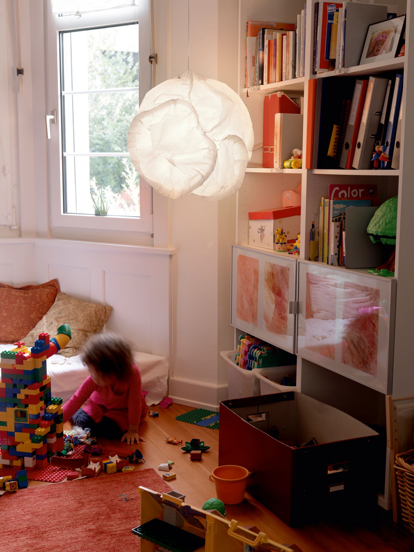 Kinderzimmer mit Belux Cloud LED Pendelleuchte, spielendem Kind und bunten Legosteinen auf einem roten Teppich.