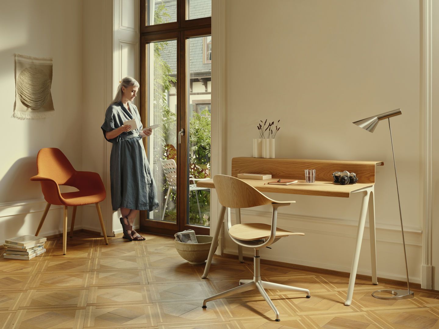 Heller Raum mit Vitra Schreibtisch Courier aus Holz, Stuhl und Stehlampe. Frau am Fenster.