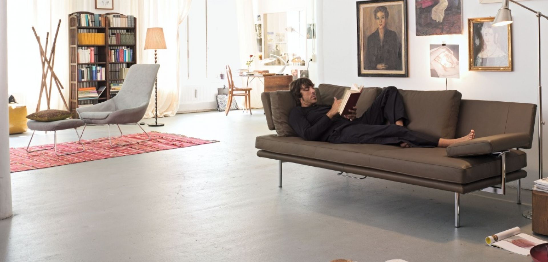 Mann liest auf braunem Walter Knoll LIVING PLATFORM Sofa mit Funktionsarmlehnen in modernem Wohnzimmer.
