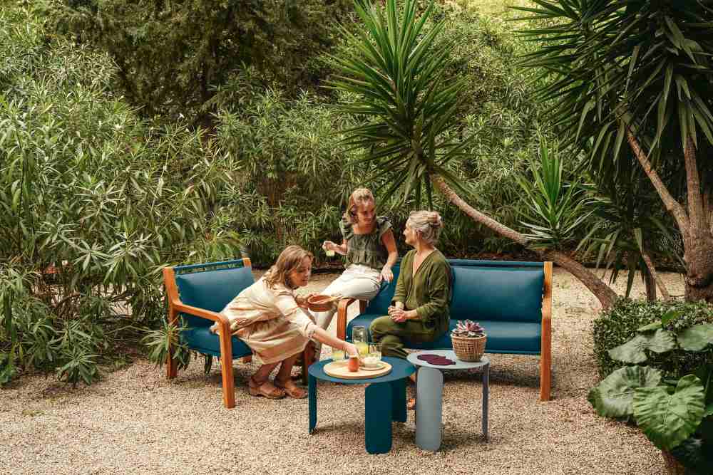 Drei Frauen sitzen im Garten auf einem blauen Somerset Sessel von Fermob und genießen die Zeit.