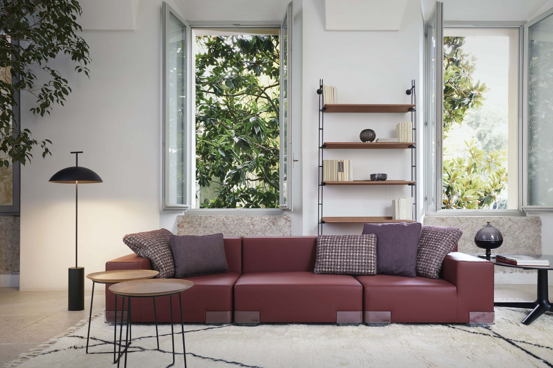 Wohnzimmer mit rotem Sofa, Beistelltischen und Adam Wood Regal mit schwarzer Esche von Kartell.