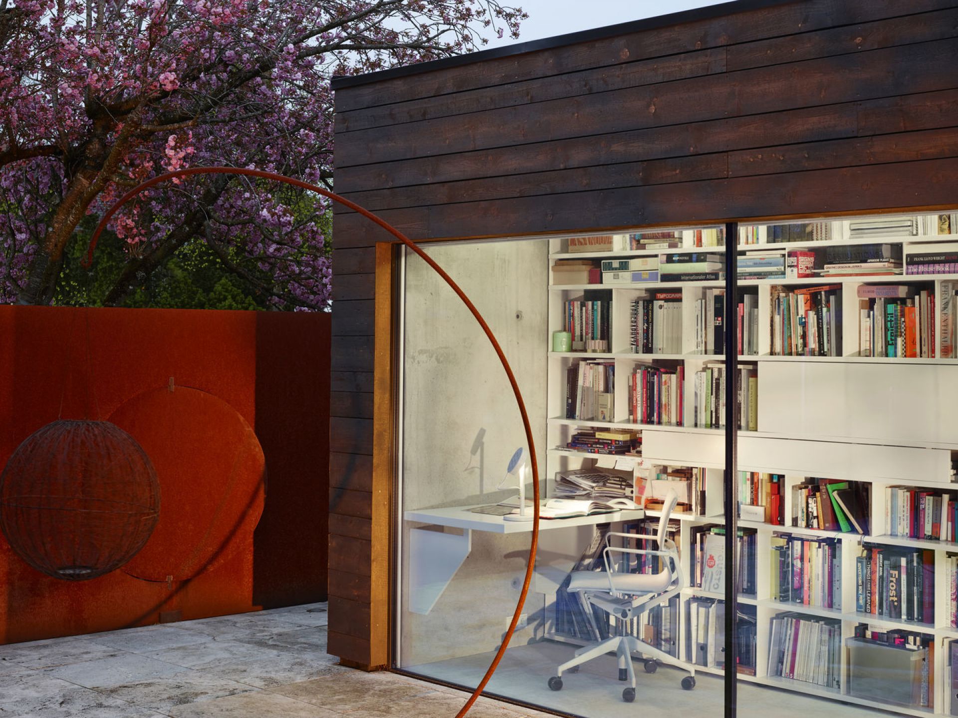 Vitra Physix Studio Bürodrehstuhl in weiß vor Bücherregal und modernem Bürogebäude mit Garten.