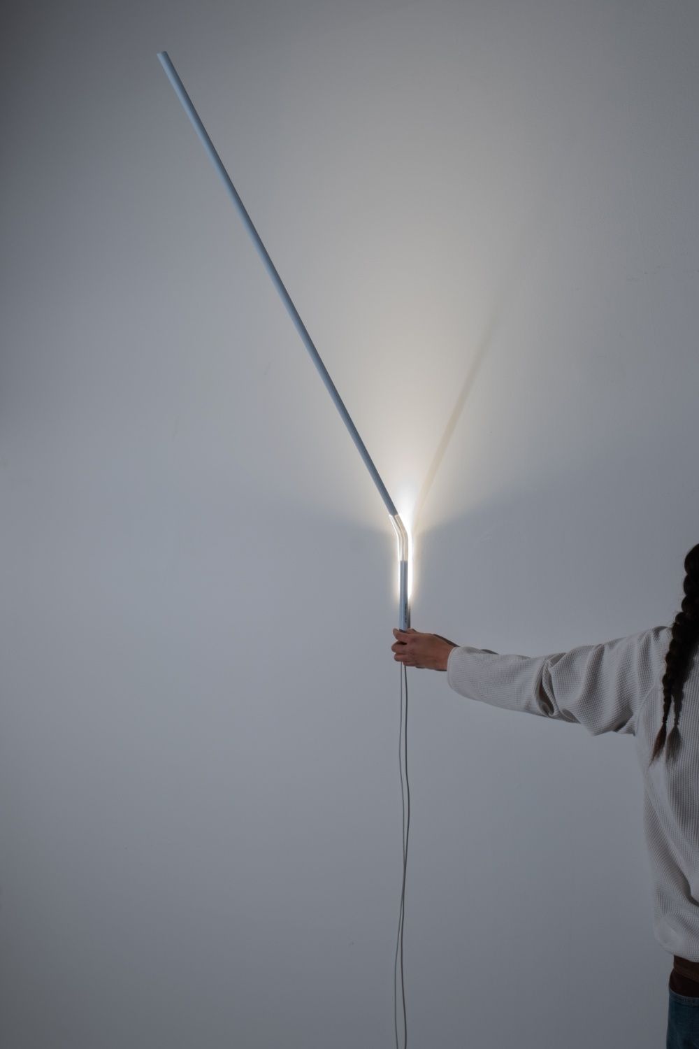Weiße Measure Light Wandleuchte von Ingo Maurer an einer Wand, gehalten von einer Person.