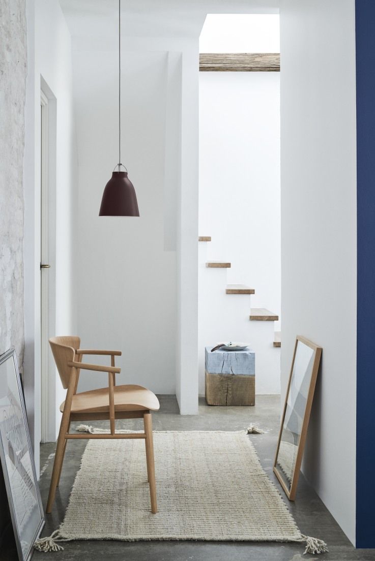 Moderne Caravaggio Pendelleuchte von Fritz Hansen in dunklem Rotbraun über einem hellen Wohnbereich mit Holzstuhl.