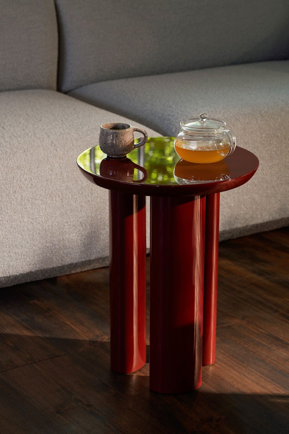 Couchtisch rot mit Teekanne und Tasse vor grauem Sofa. Wohnzimmer Möbel.