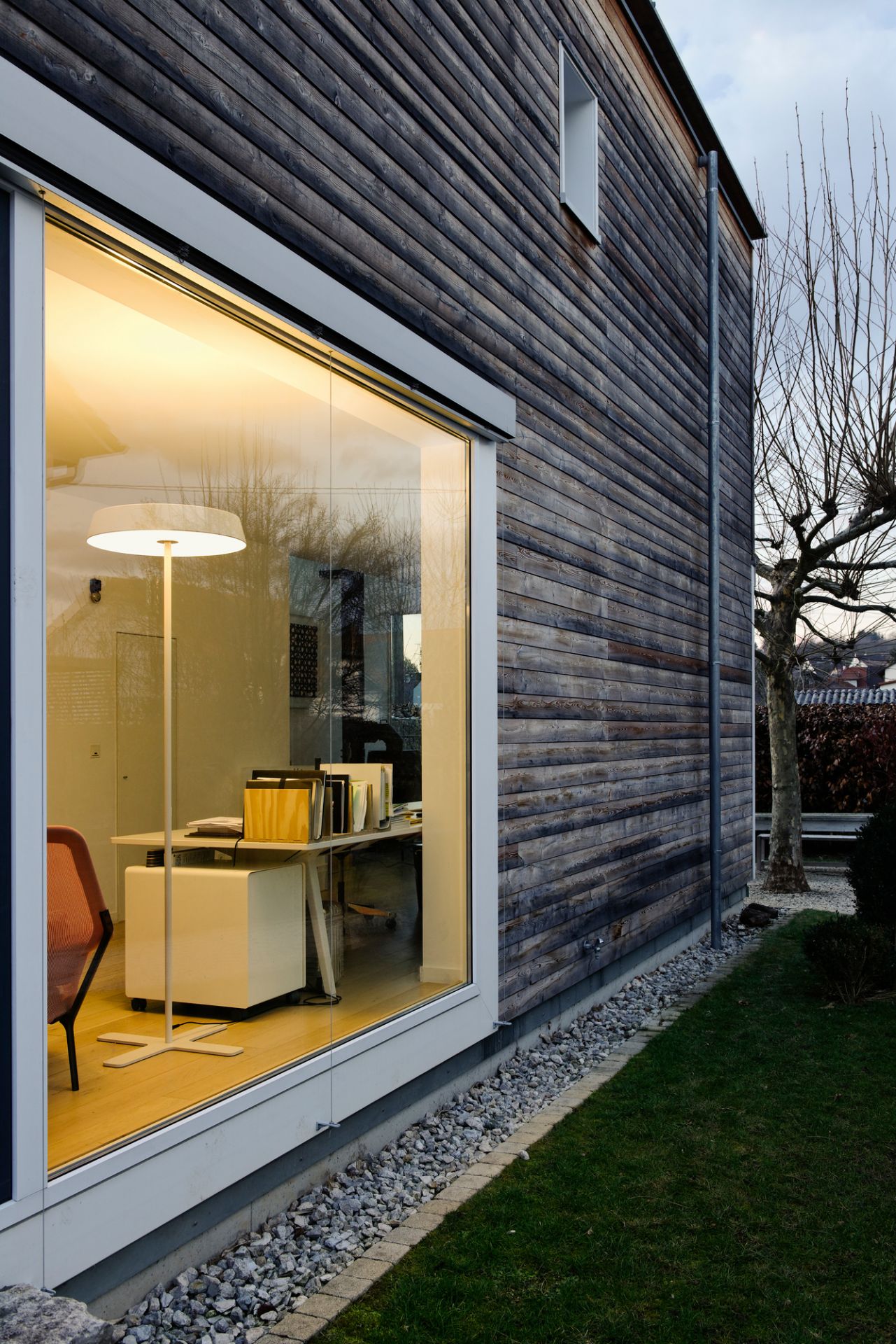 Koi S LED Stehleuchte von Belux, gesehen durch ein Fenster, beleuchtet einen modernen Arbeitsbereich.