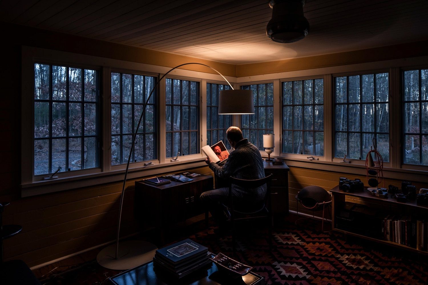 Mann liest unter der Twiggy Stehleuchte von Foscarini in einem gemütlichen, rustikalen Arbeitszimmer mit Blick auf den Wald.