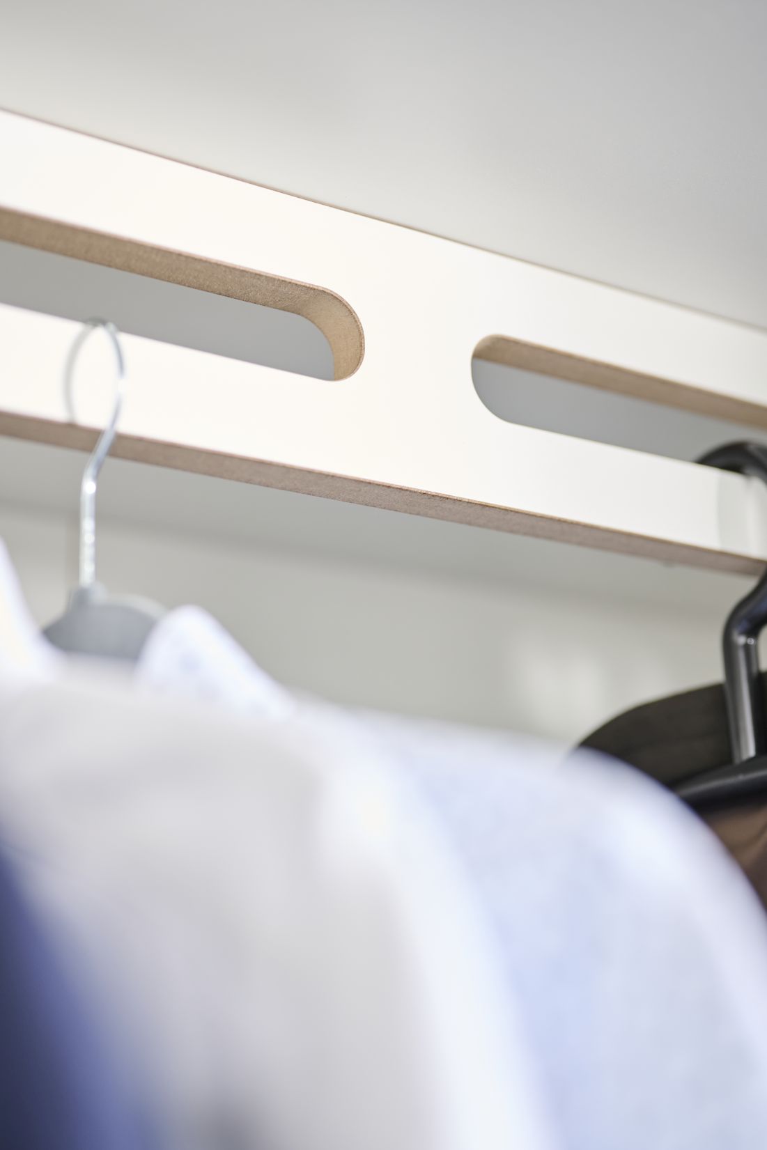 Detailaufnahme Tojo Schrank Grundmodul: Weiße Schrankleiste mit Aussparungen für Kleiderbügel, modernes Schranksystem.