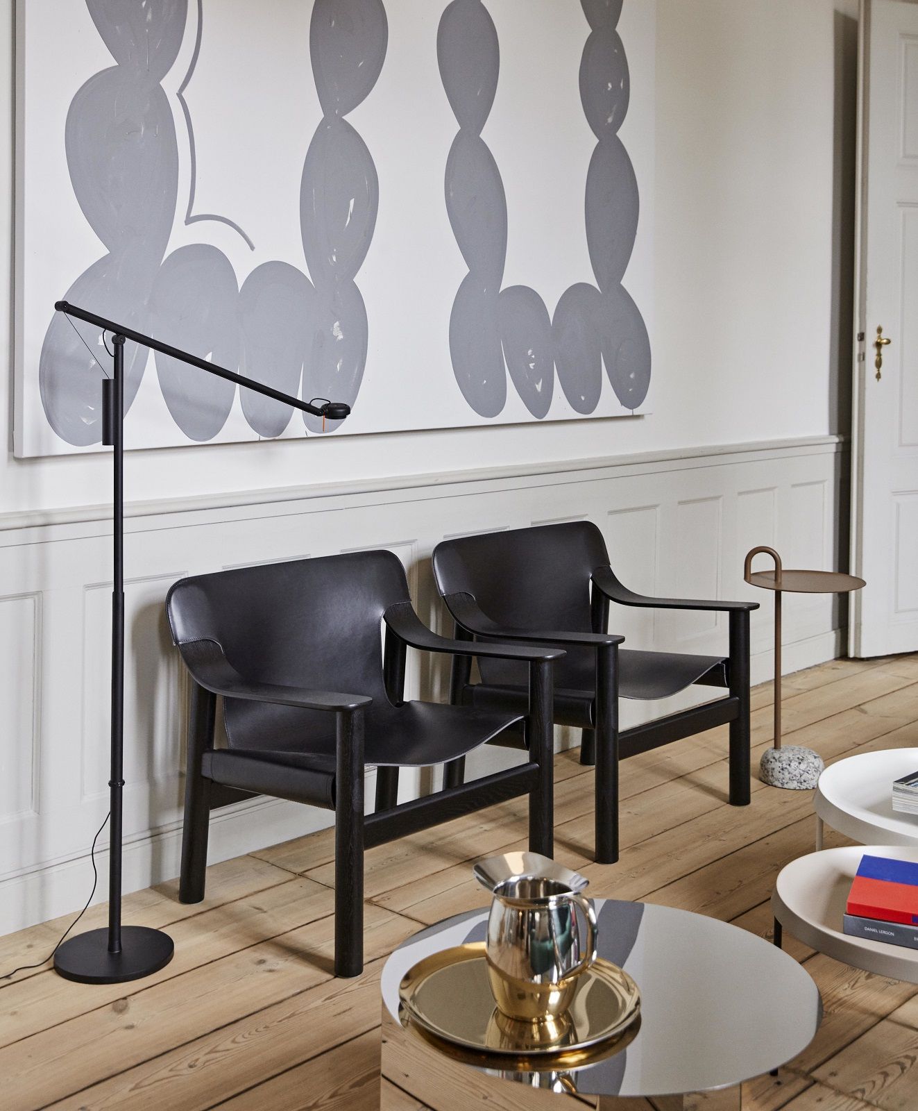 Wohnzimmer-Szene mit Hay Bowler Beistelltisch aus Stahl und Marmor neben schwarzen Sesseln und Stehlampe.